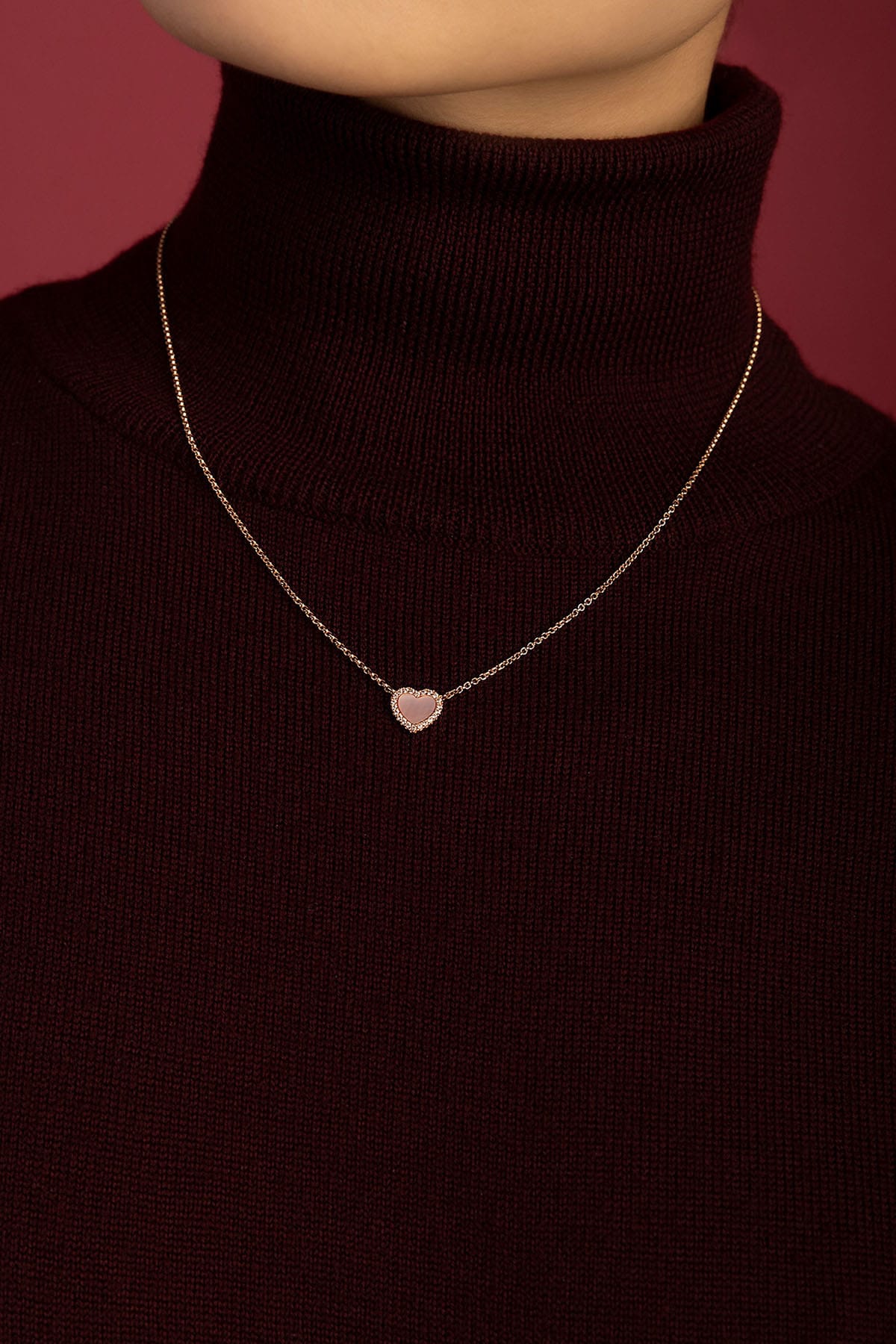 Woman wearing APM heart necklace, a tender glow against burgundy warmth.