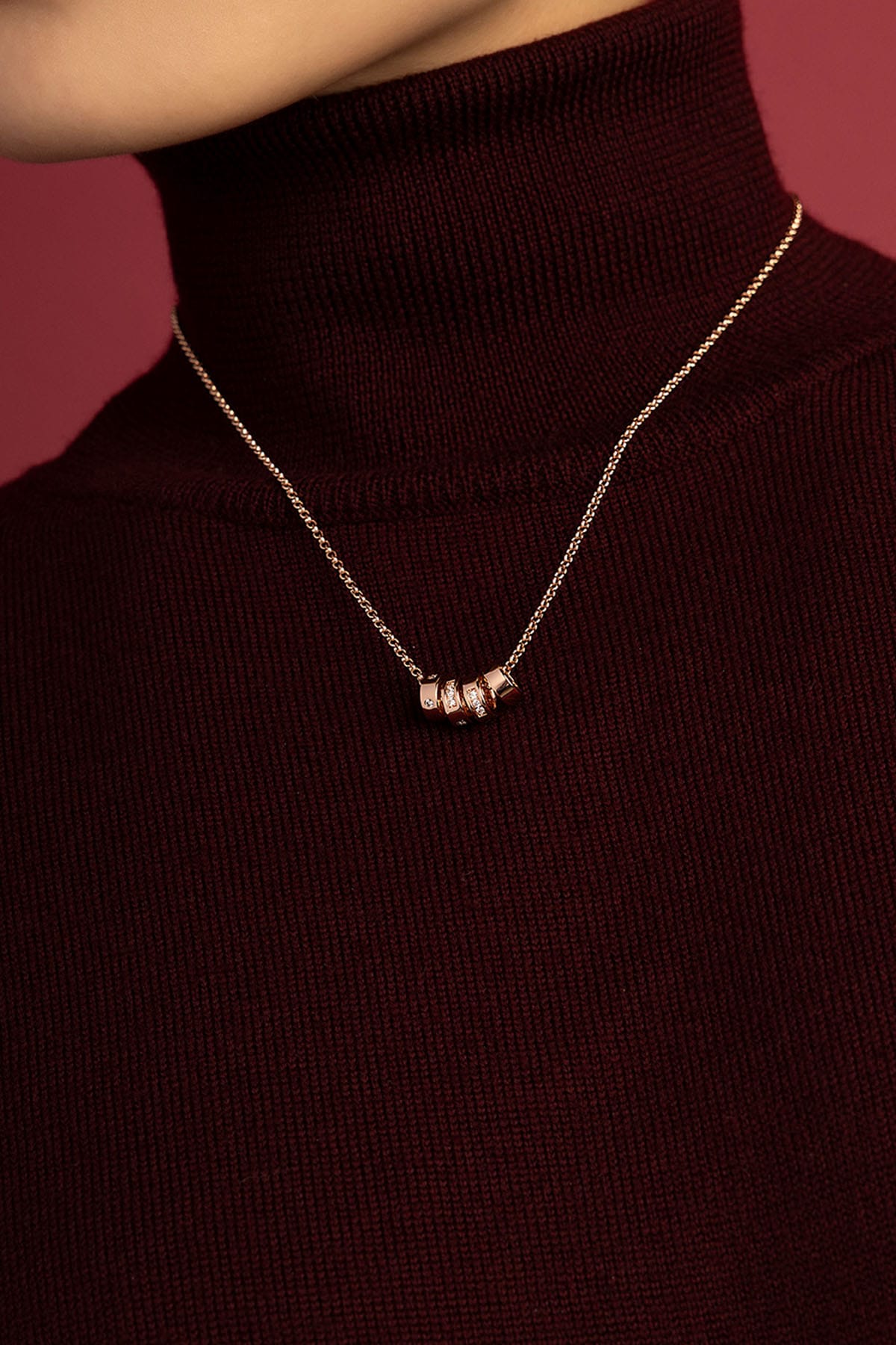 Woman wearing APM Monaco necklace, delicate charms glowing against burgundy warmth.