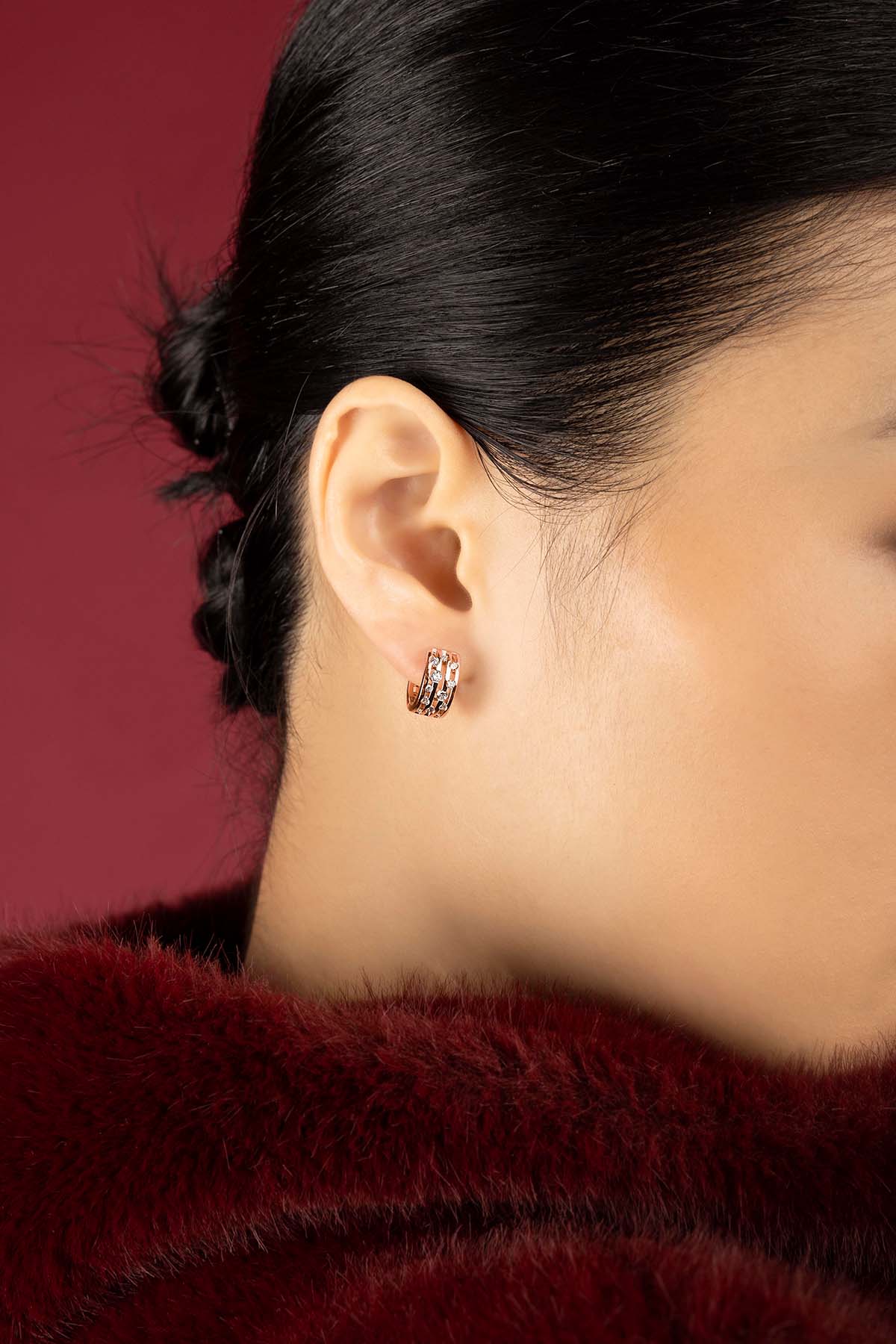 Woman wearing APM Monaco hoop earrings, a warm rose glow against crimson elegance.