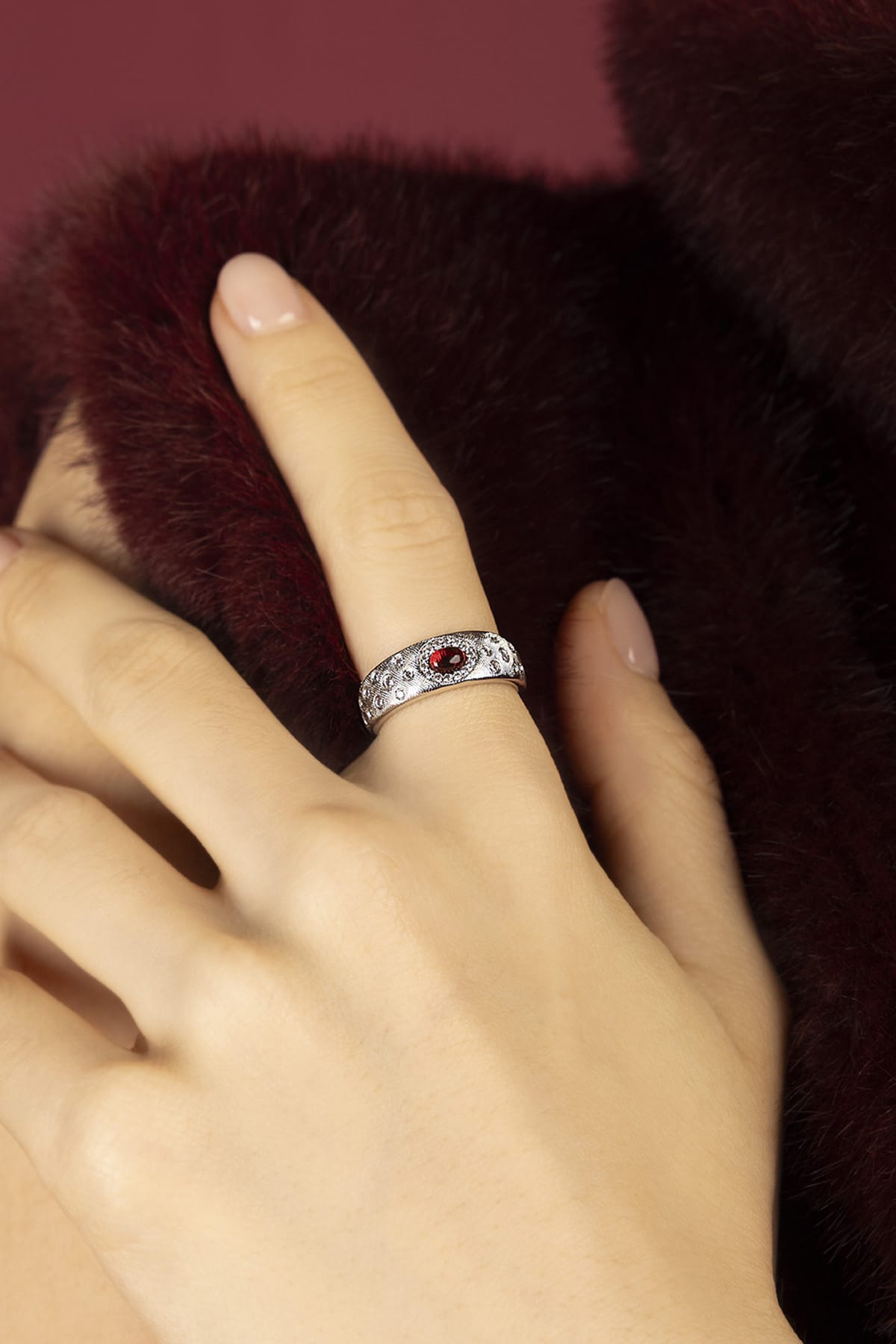 Woman wearing APM Monaco ring, a red spark against velvet warmth.