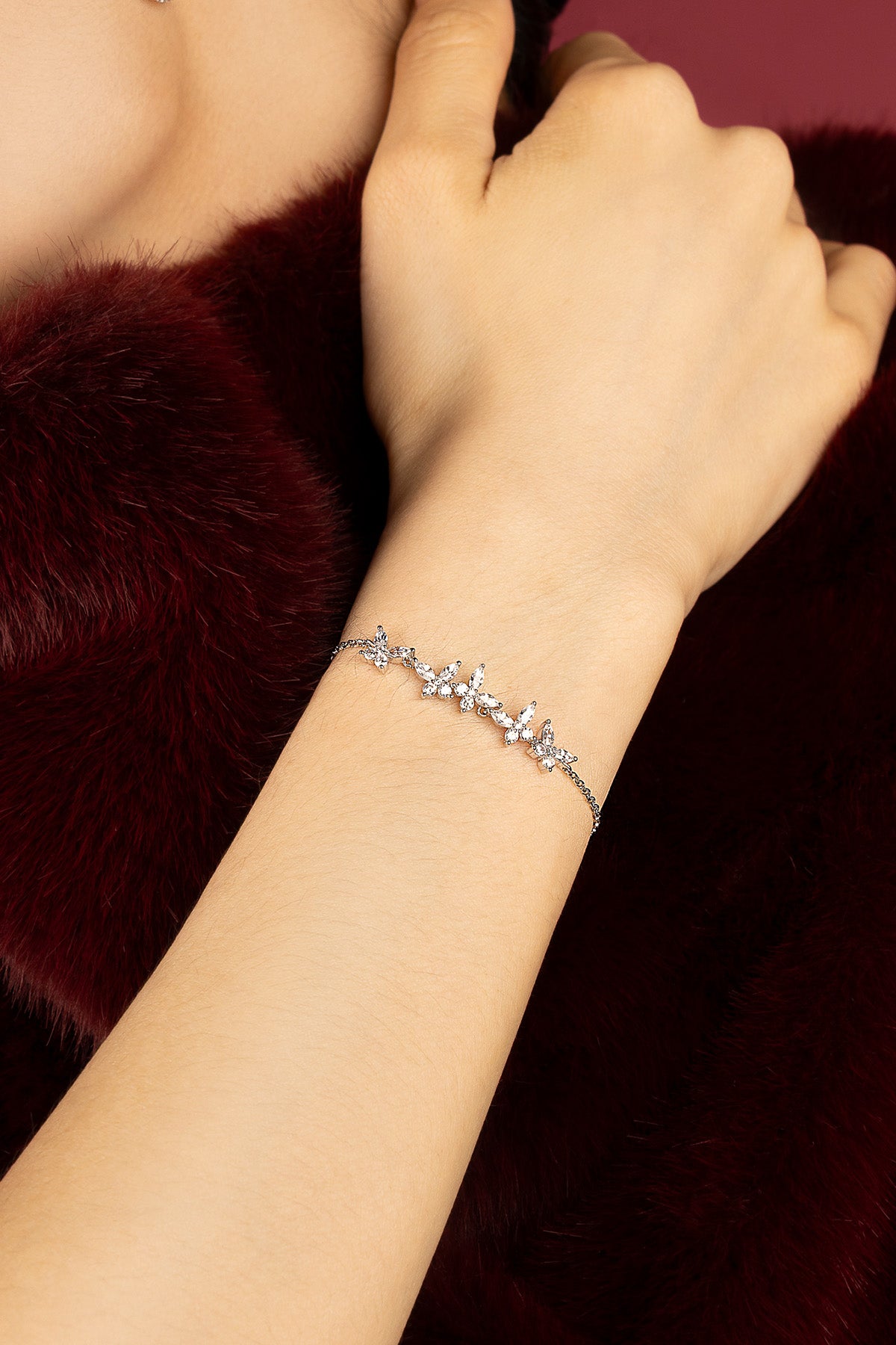 Woman wearing APM butterfly bracelet, a delicate flutter of light against burgundy softness.