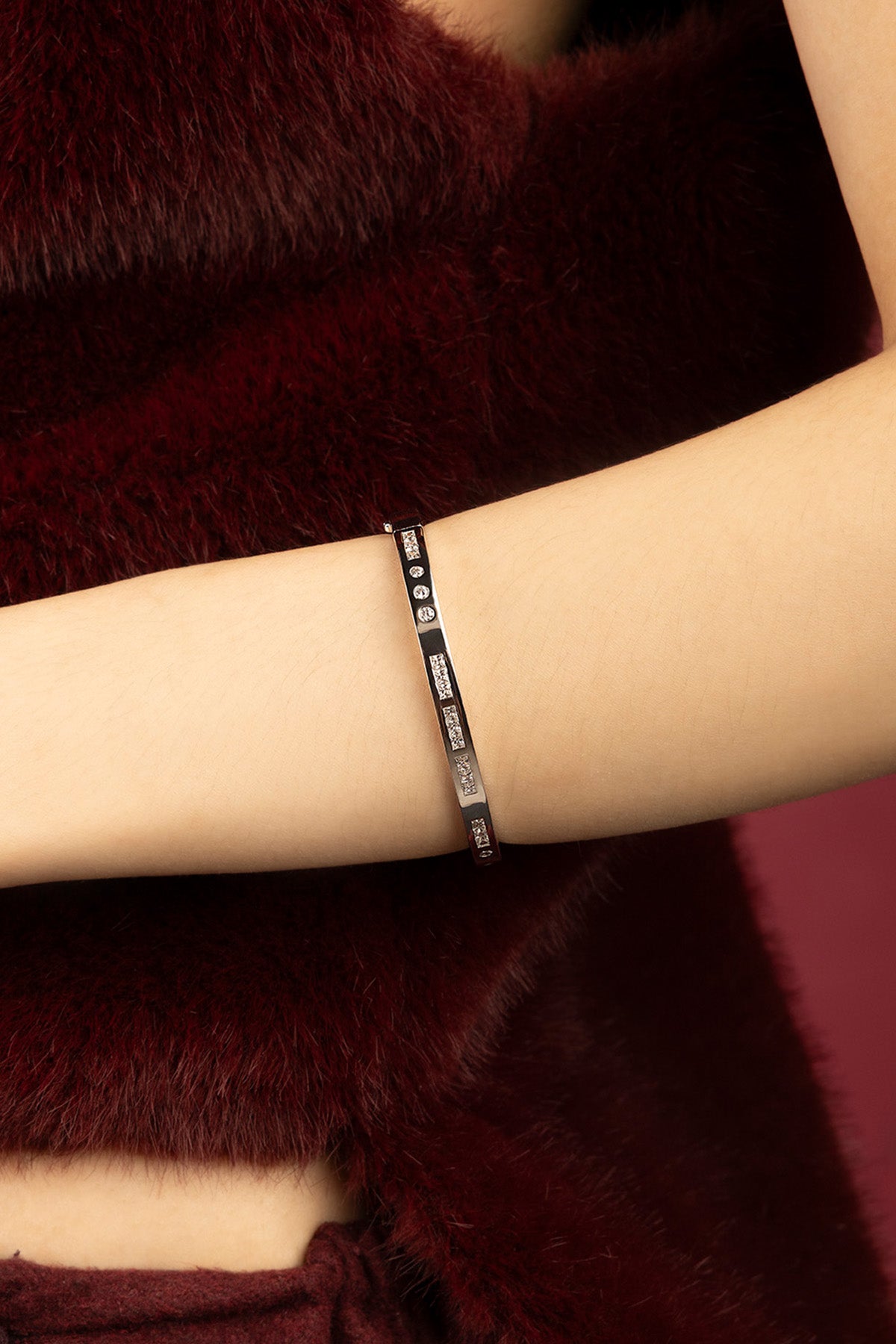 Woman wearing APM Monaco bangle, a sleek shimmer against burgundy warmth.