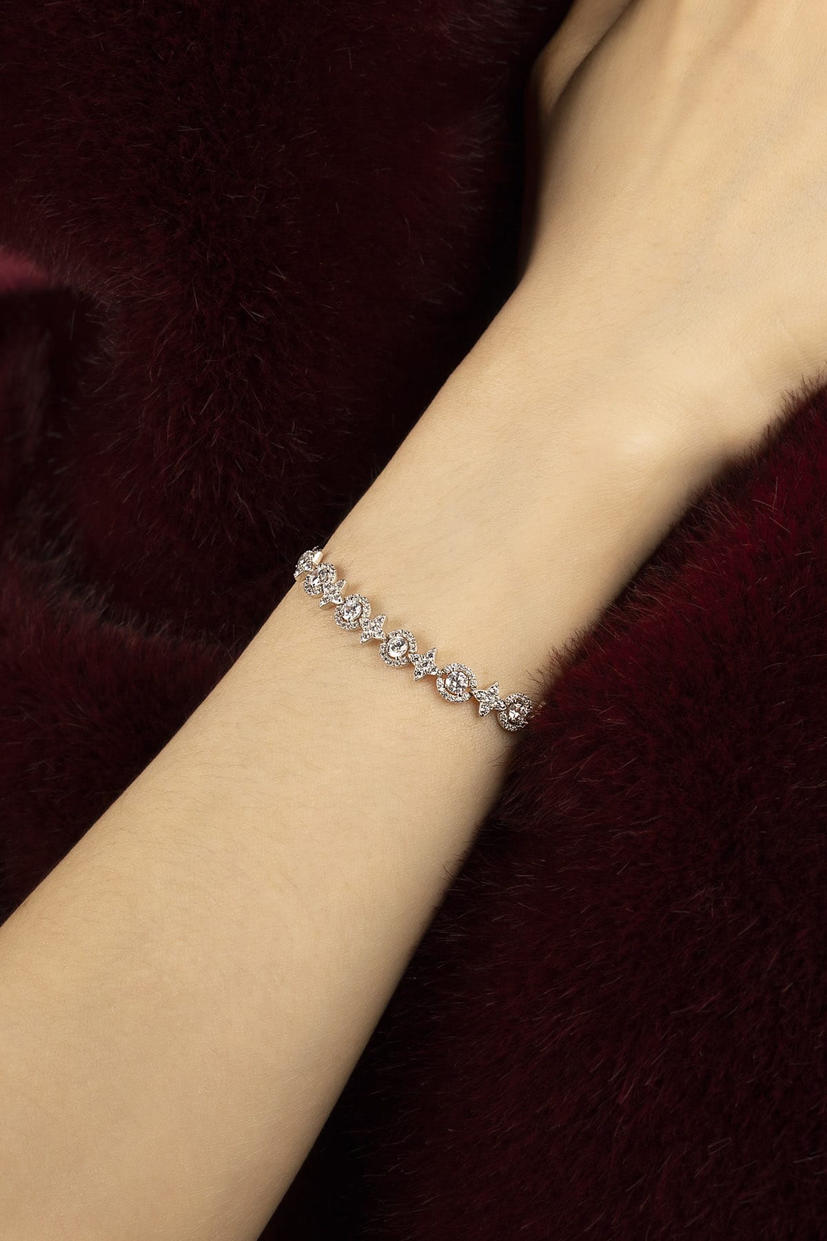 Woman wearing APM bracelet, a delicate sparkle against plush burgundy.