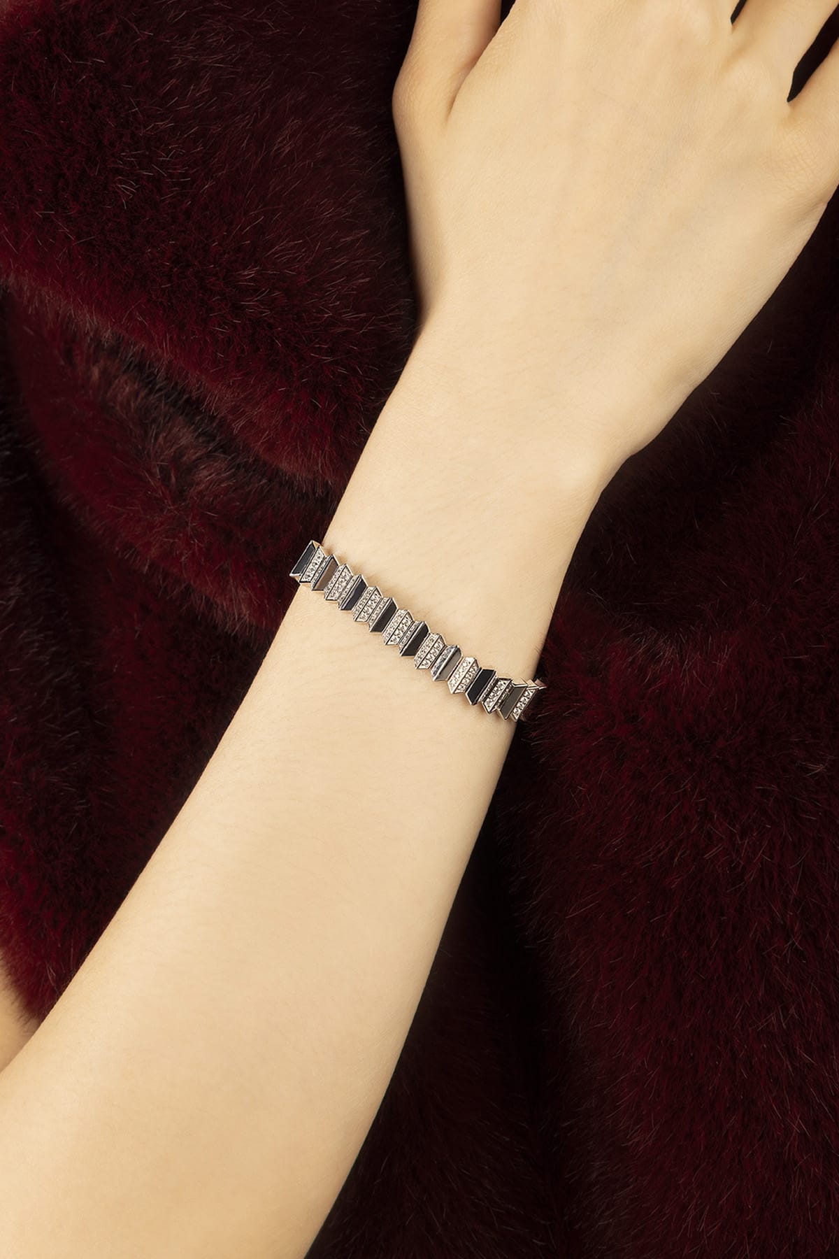 Woman wearing APM bracelet, a sharp geometric statement against plush burgundy.