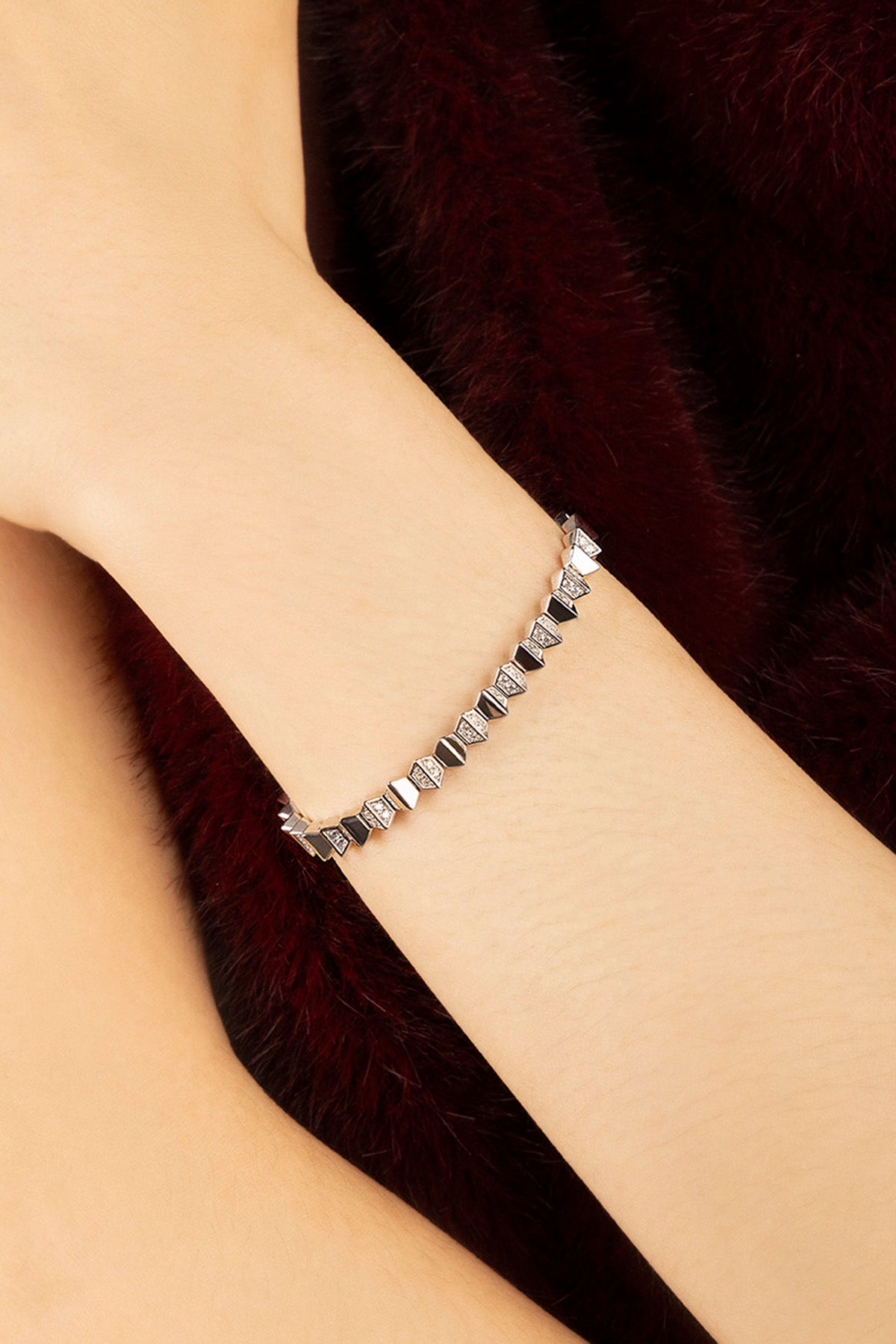 Woman wearing APM Bracelet, a delicate spark of geometry against velvet warmth.