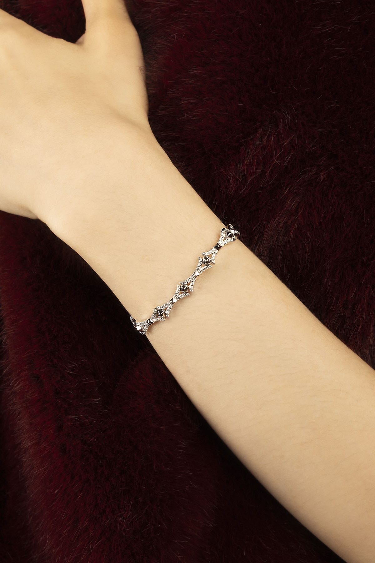 Woman wearing APM bracelet, a delicate sparkle against deep velvet elegance.