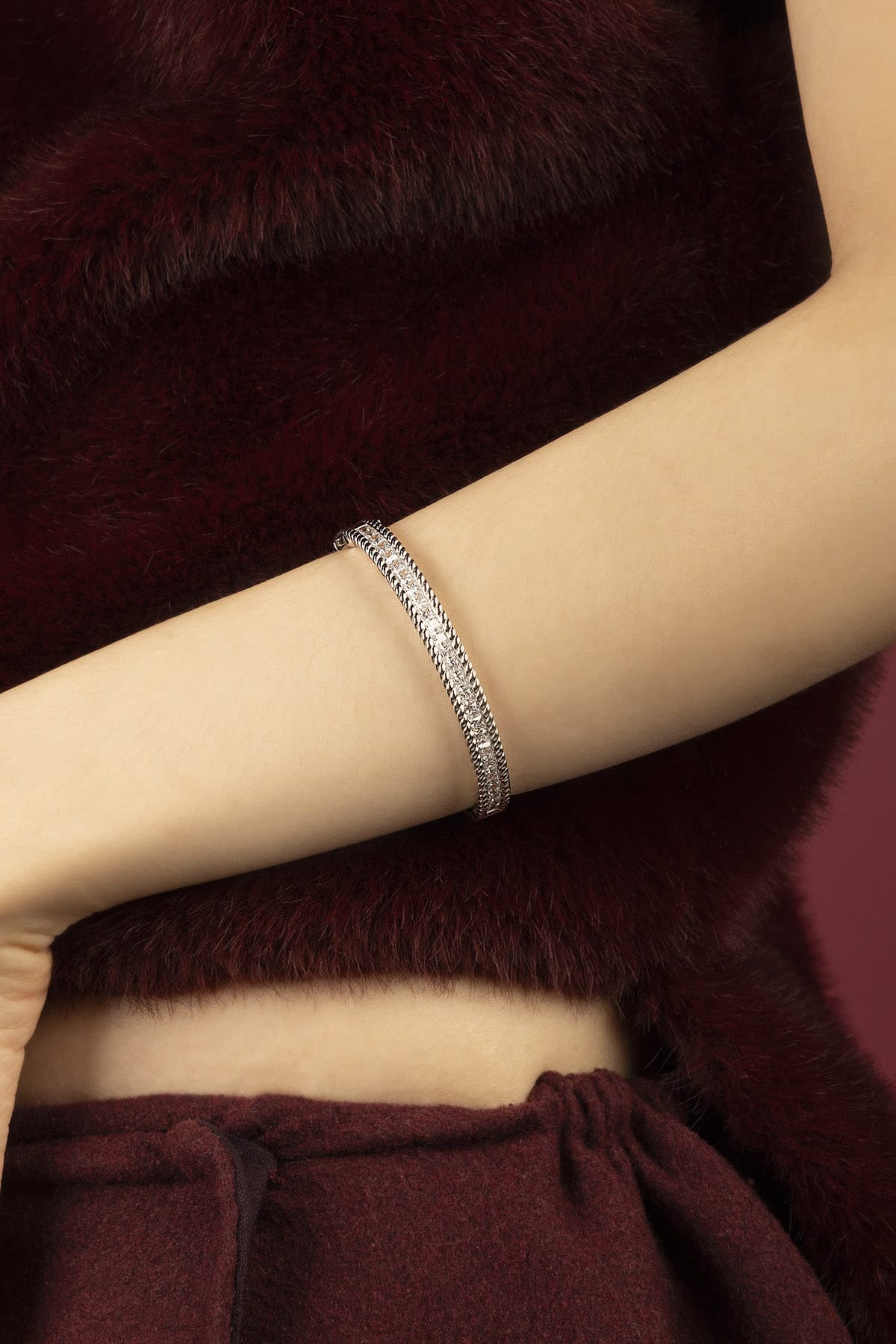 Woman wearing APM Monaco bangle, a shimmer of quiet elegance against burgundy.