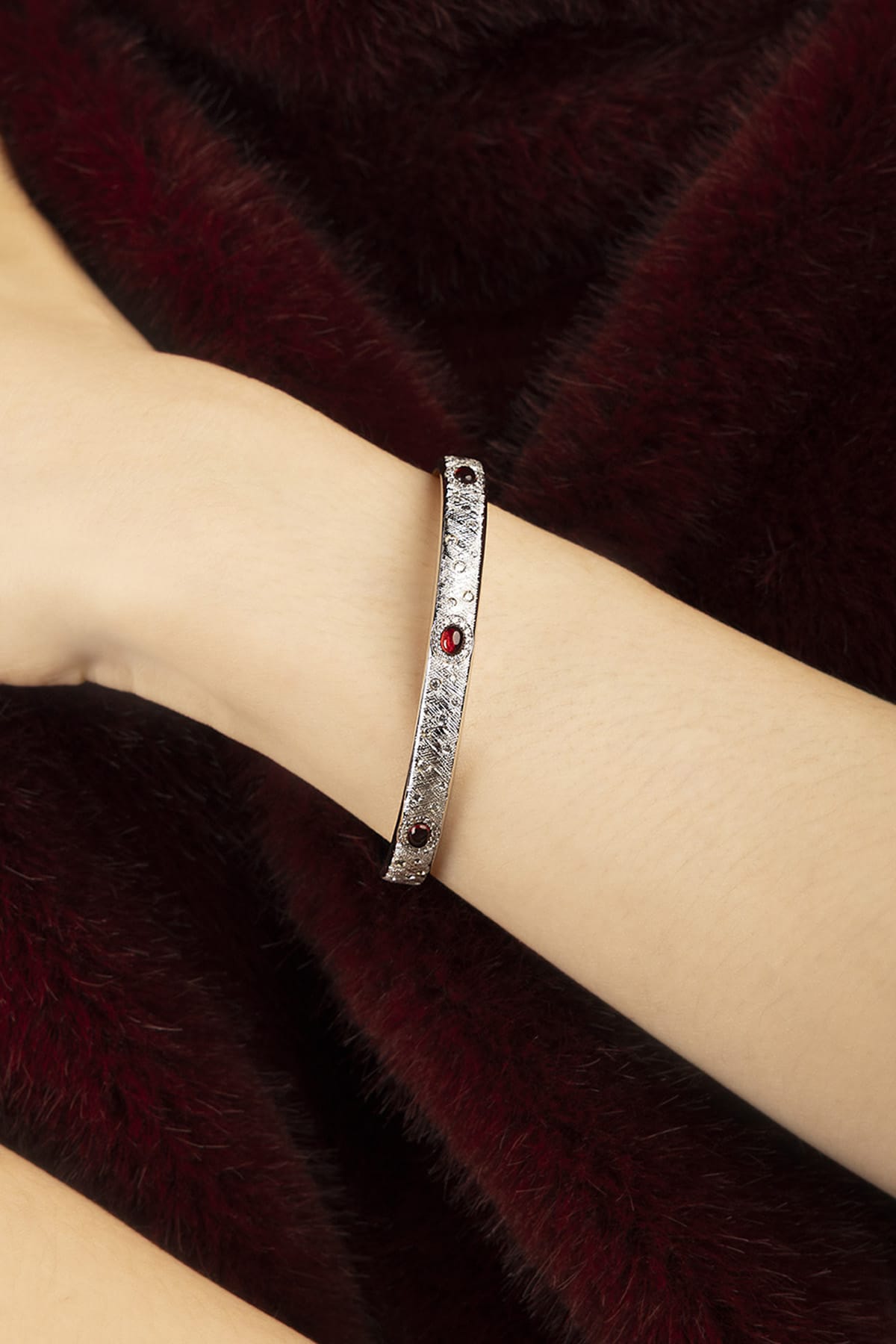 Woman wearing APM bangle, rhodium finish glowing against velvet warmth, quietly bold.