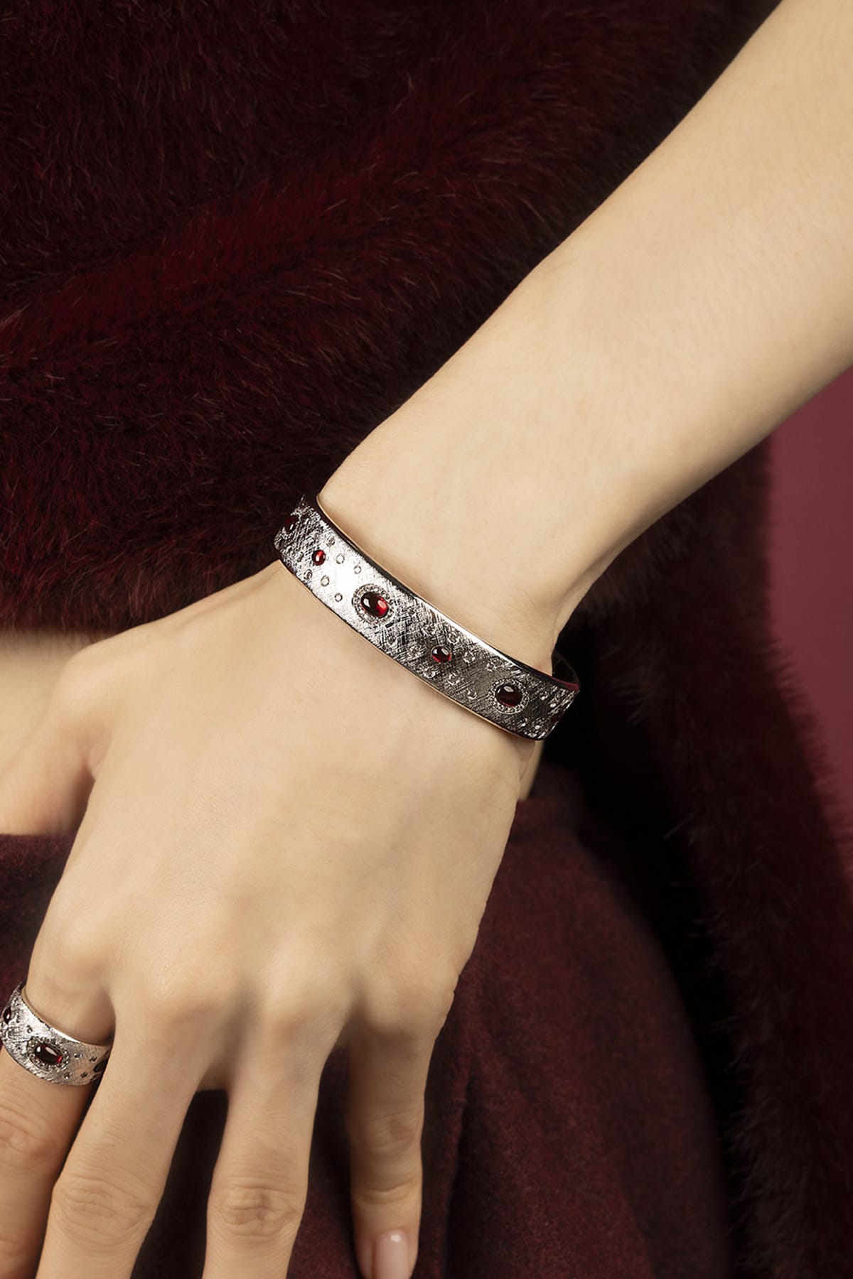 Woman wearing APM Monaco bangle, rhodium finish glowing with deep red allure.