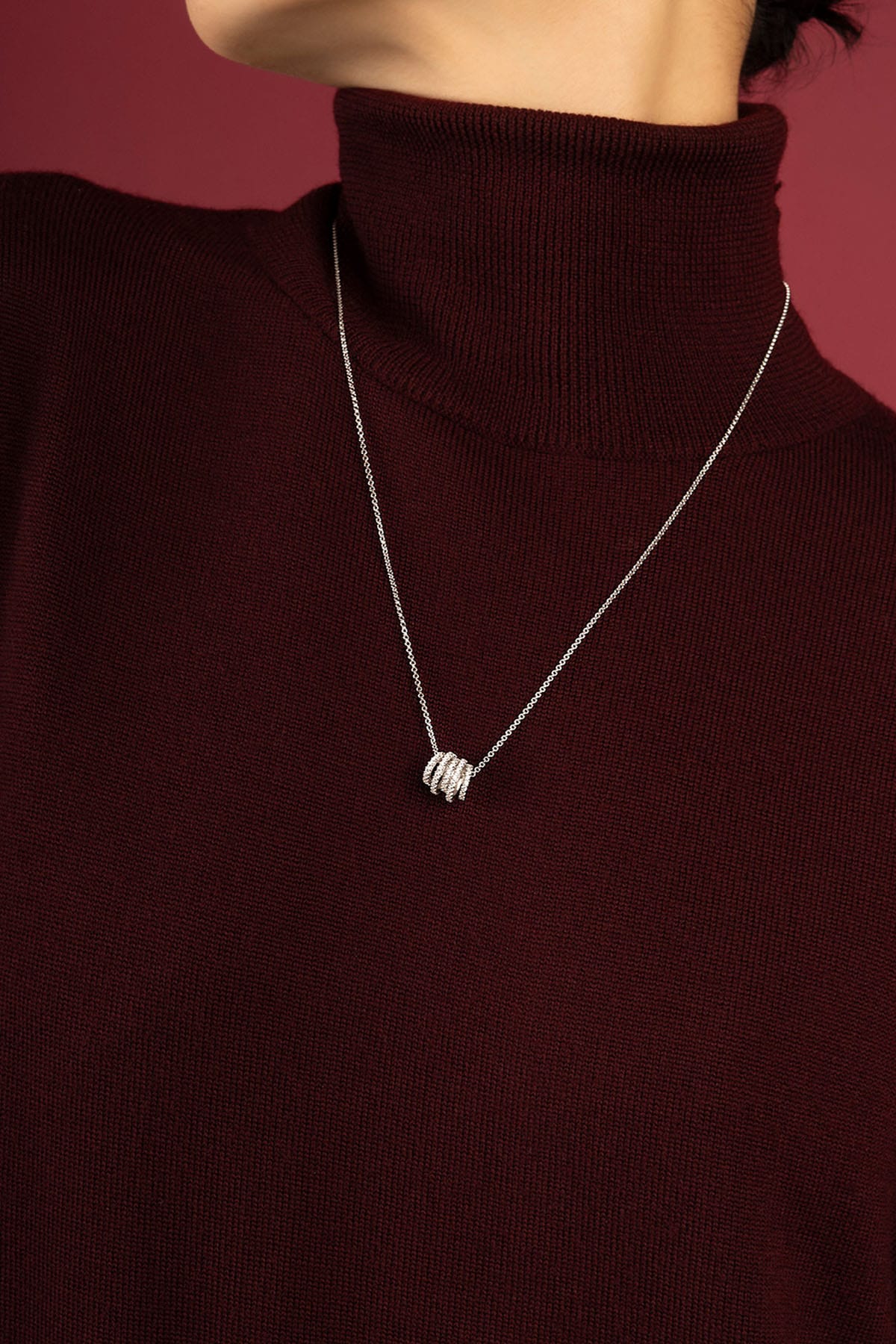 Woman wearing APM Monaco necklace, delicate rhodium finish charm resting on burgundy knit.