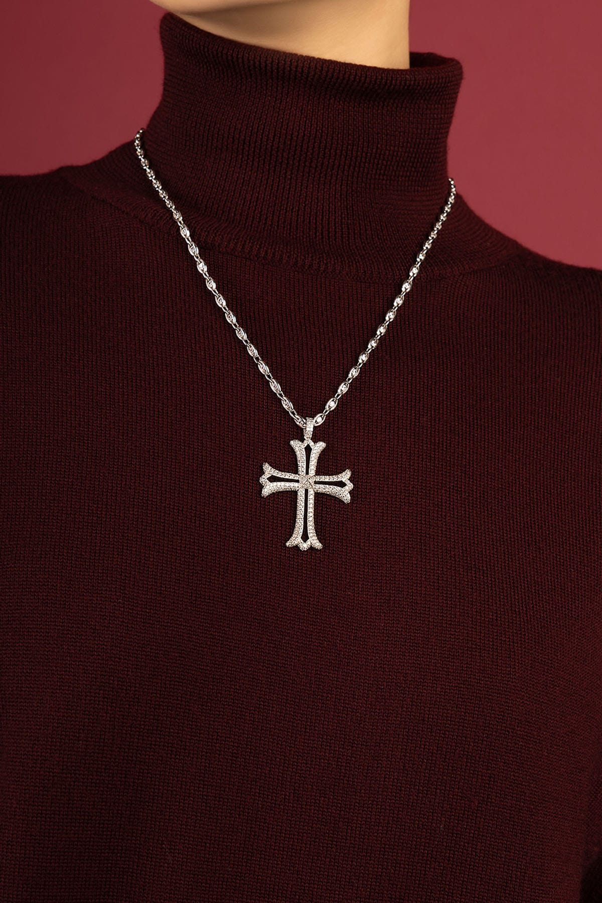 Woman wearing APM cross necklace, a bold statement over burgundy knitwear.