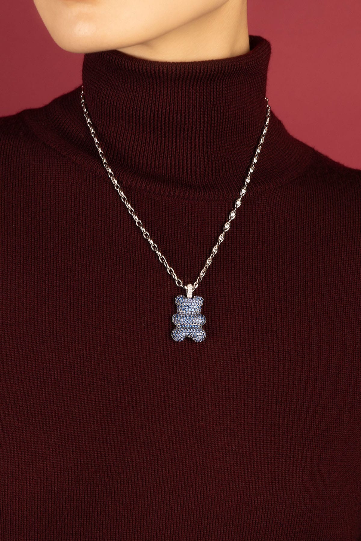 Woman wearing APM Yummy Bear Necklace, a playful blue statement on cozy burgundy.