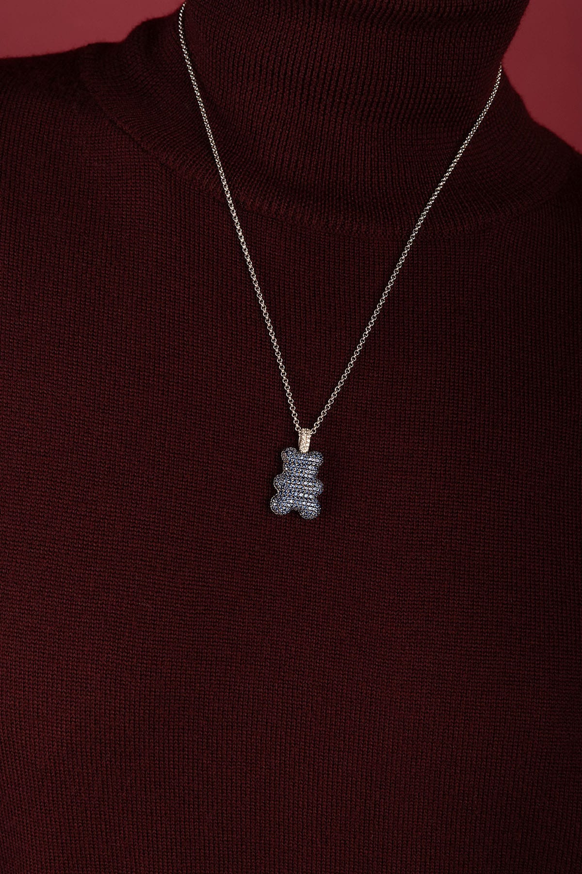 Woman wearing APM bear pendant necklace, a playful charm on burgundy knitwear.