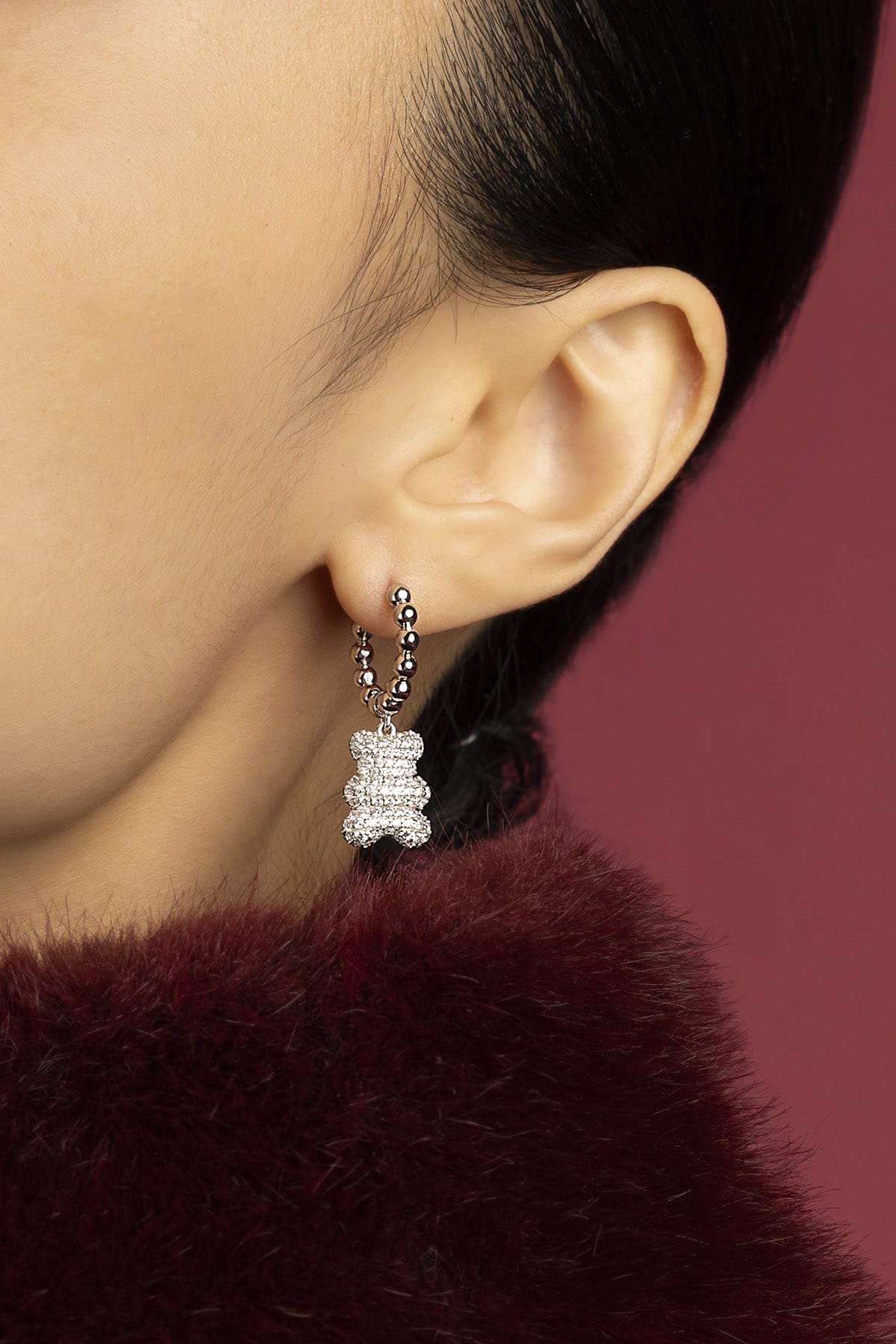 Woman wearing APM bear hoop earrings, a playful sparkle against burgundy warmth.