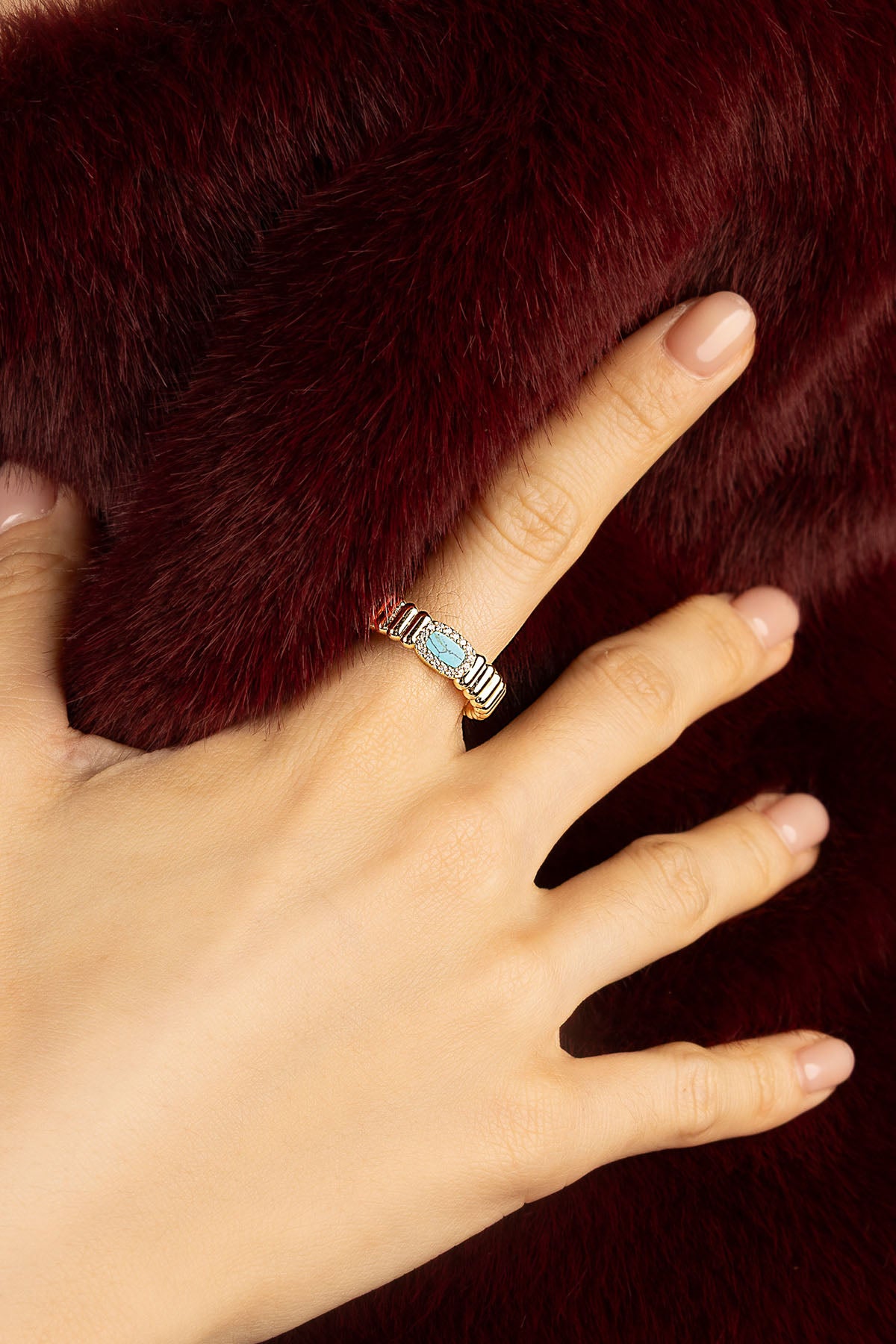Woman wearing APM Monaco ring, turquoise glow against rich velvet warmth.