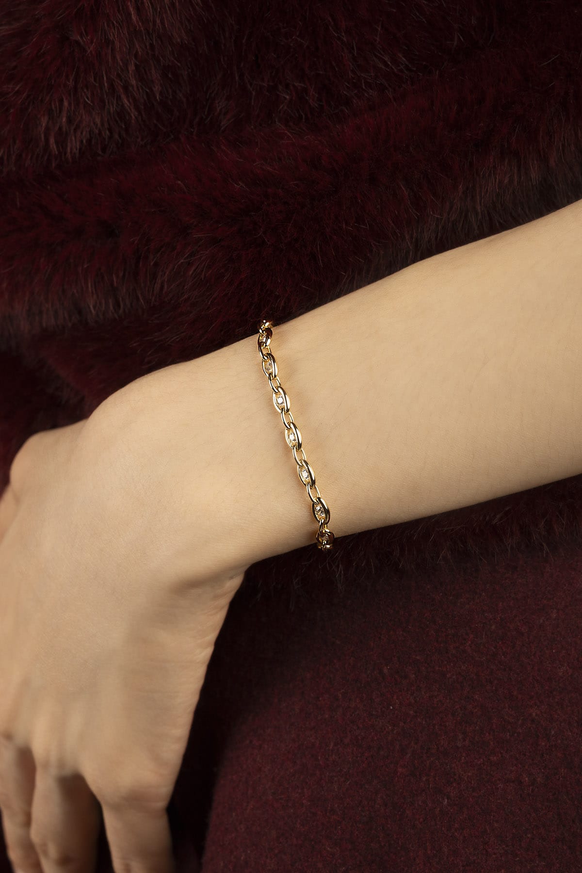 Woman wearing an APM chain bracelet, a golden whisper against burgundy warmth.