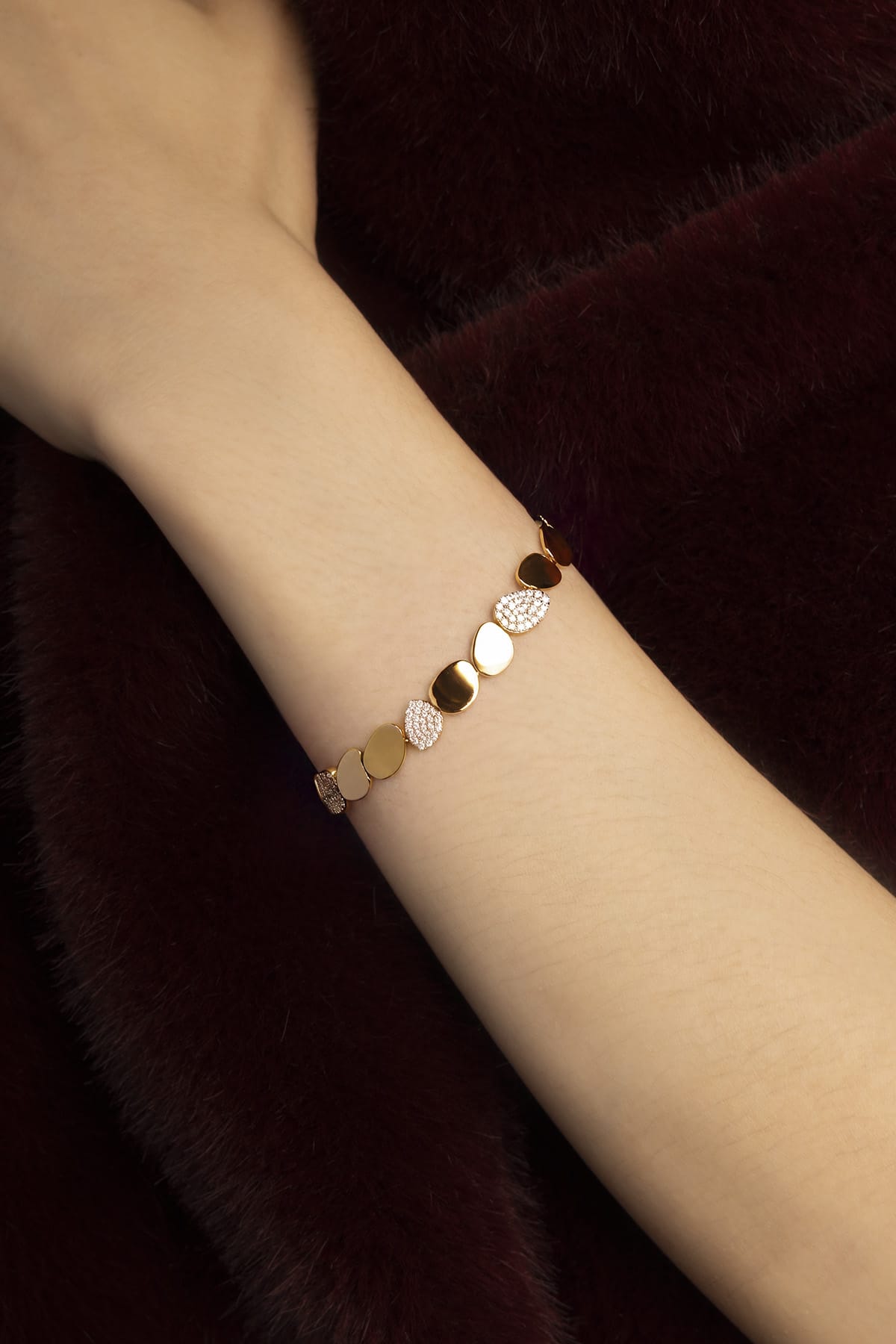 Woman wearing APM bracelet, golden pebbles glowing against plush burgundy.