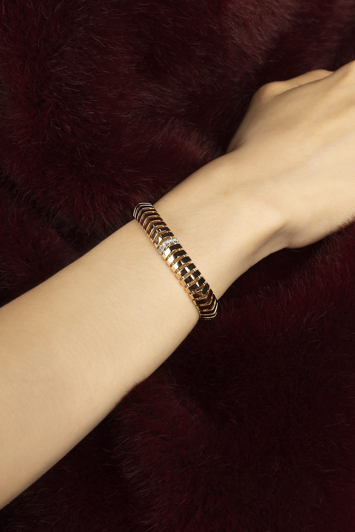 Woman wearing APM bracelet, a golden ripple of quiet confidence against velvet.
