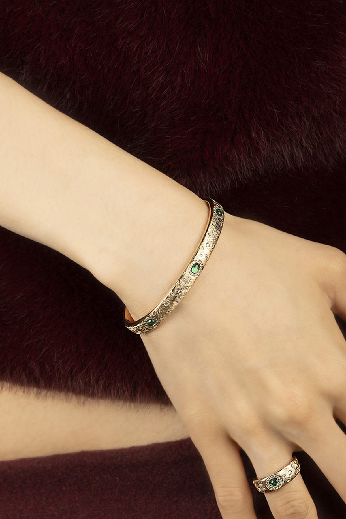 Woman wearing APM Monaco bangle, golden allure with emerald sparks, quietly regal.