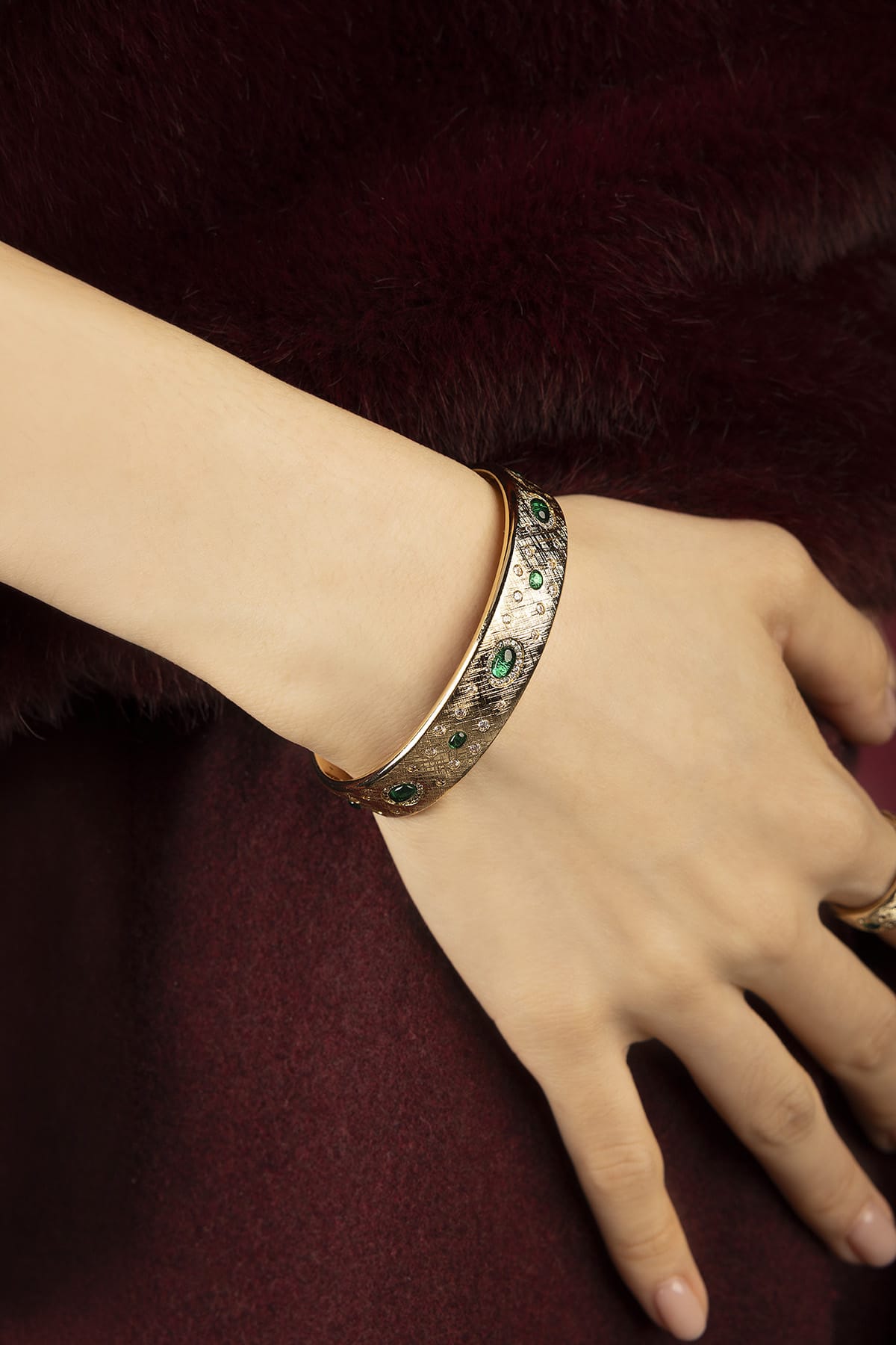 Woman wearing APM Monaco bangle, emerald whispers on a vintage-inspired glow.