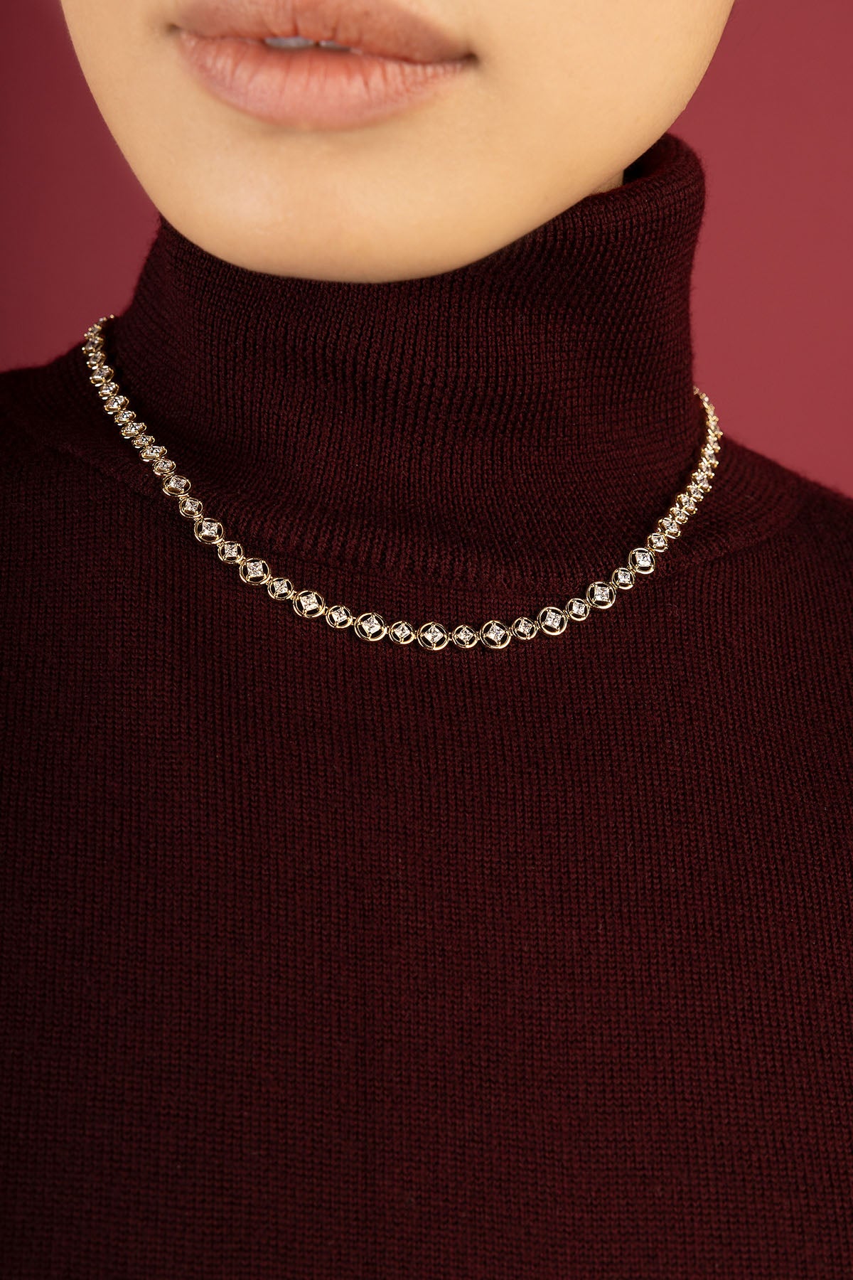 Woman wearing APM Monaco necklace, a luminous line of sparkle on burgundy.