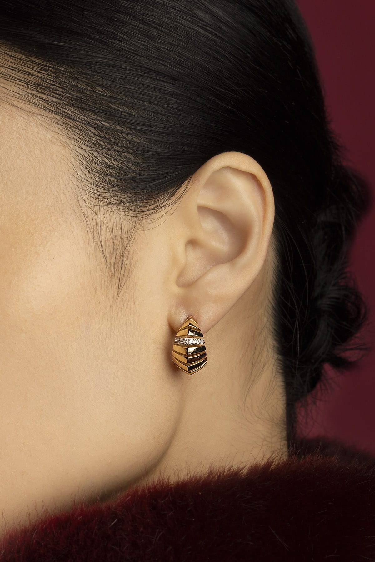 Woman wearing APM Monaco earrings, sculpted golden curves whispering quiet elegance.