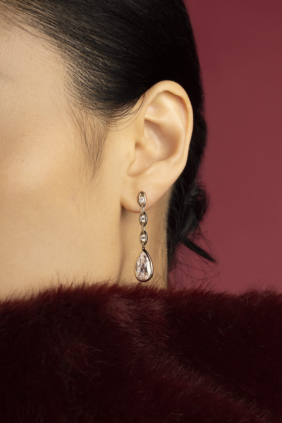 Woman wearing APM drop earrings, a whisper of crystal elegance against crimson.