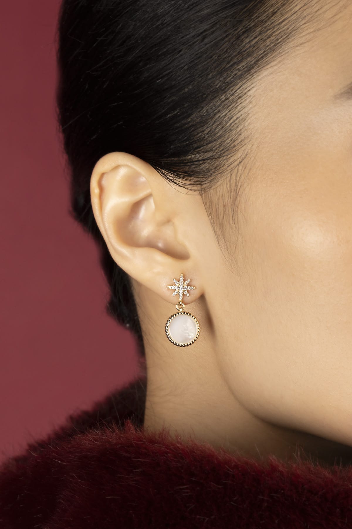 Woman wearing APM star drop earrings, a celestial glow against crimson warmth.