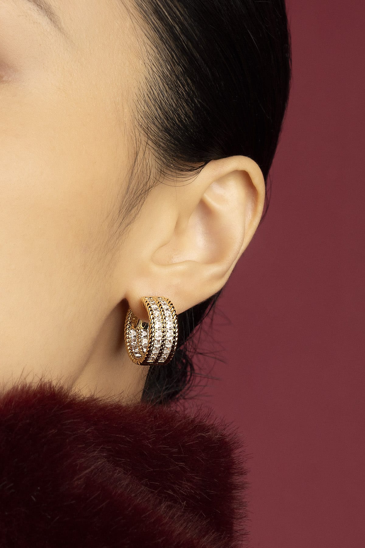 Woman wearing APM hoop earrings, a golden glow against burgundy warmth.