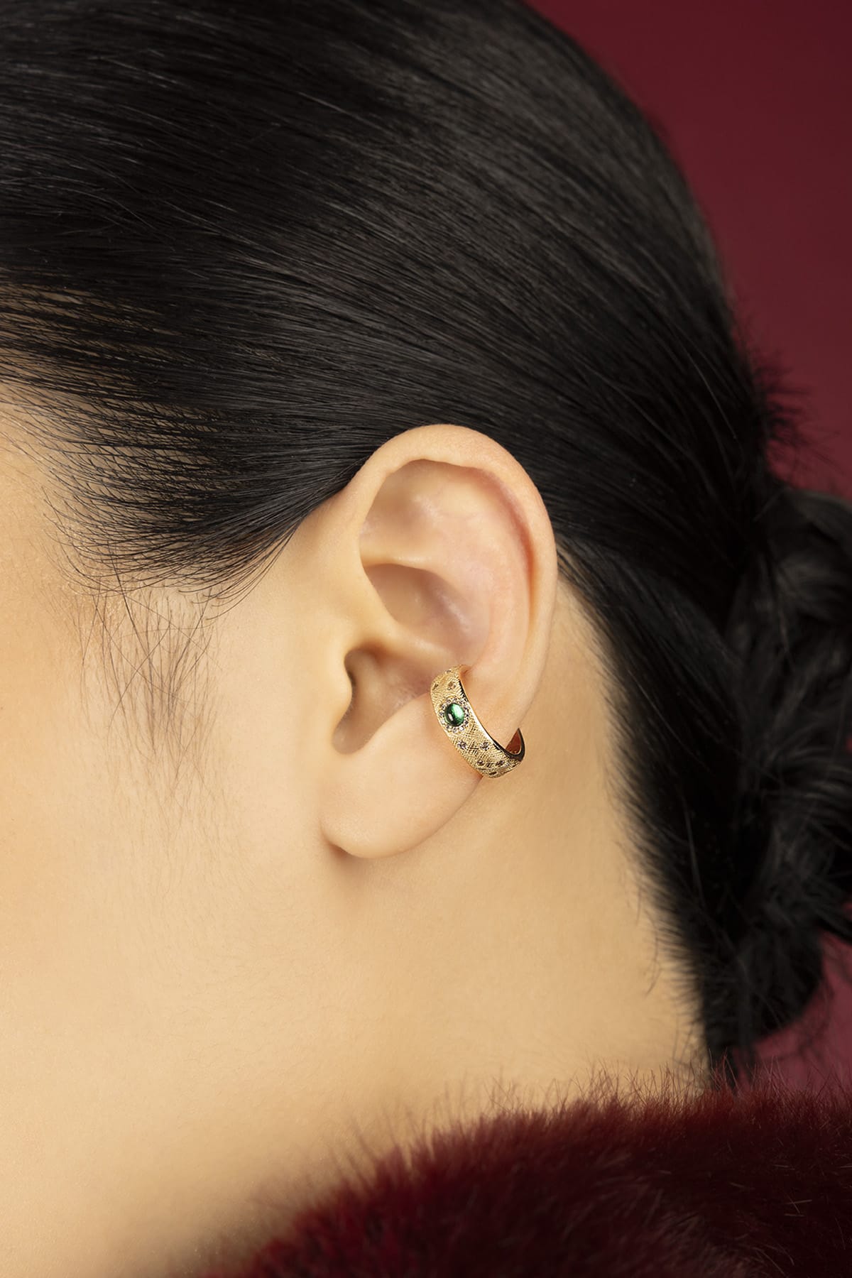 Woman wearing APM ear cuff, a golden whisper with an emerald green glow.