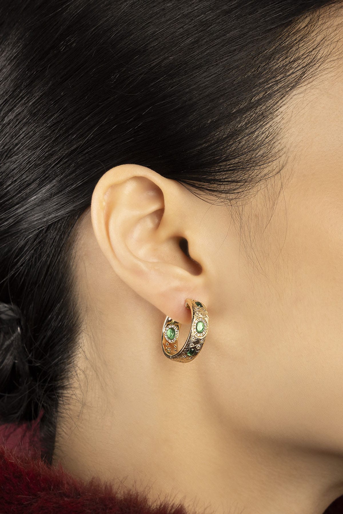 Woman wearing APM Monaco hoop earrings, green accents glowing with quiet elegance.