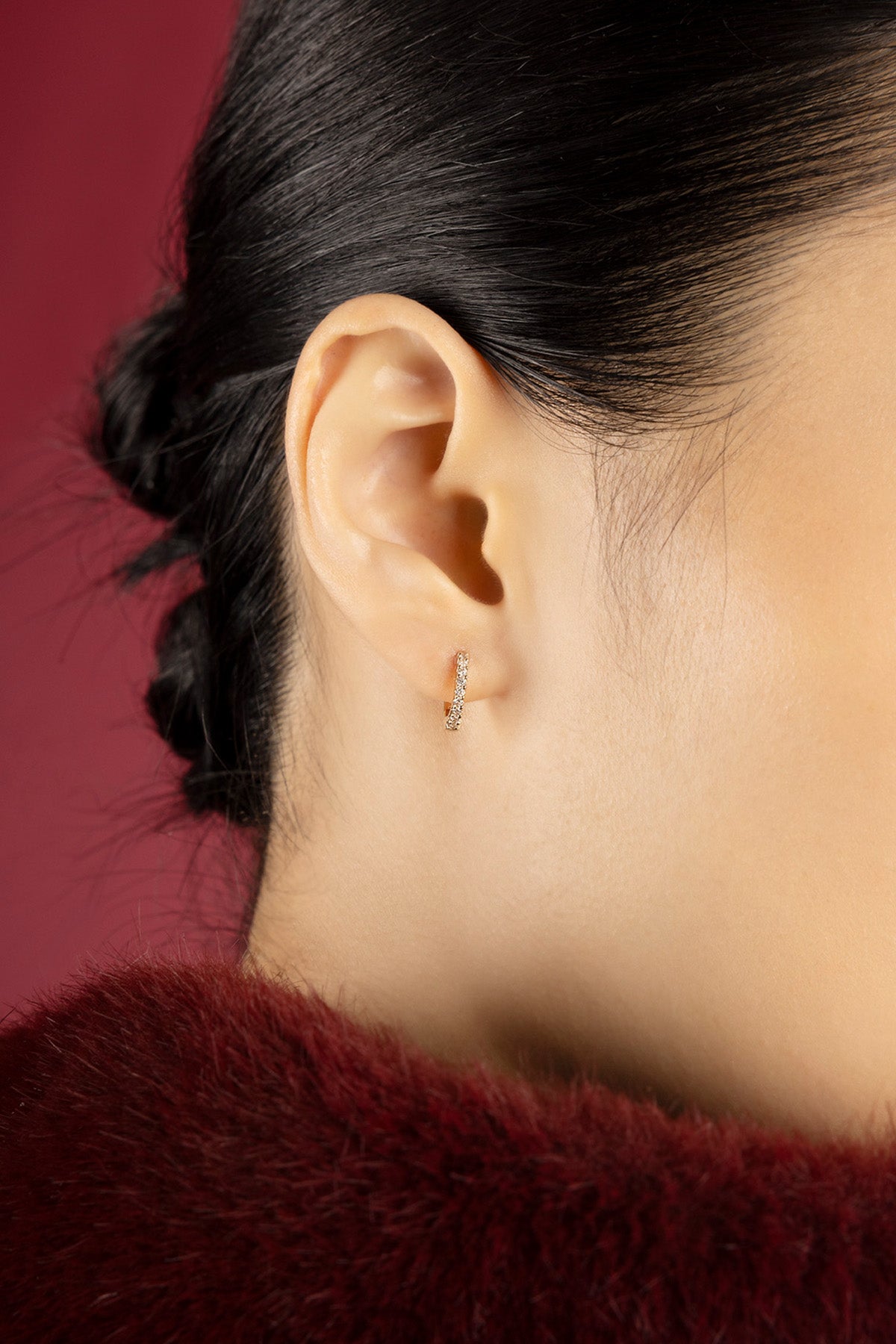 Woman wearing APM Monaco hoop earrings, a delicate sparkle against crimson warmth.