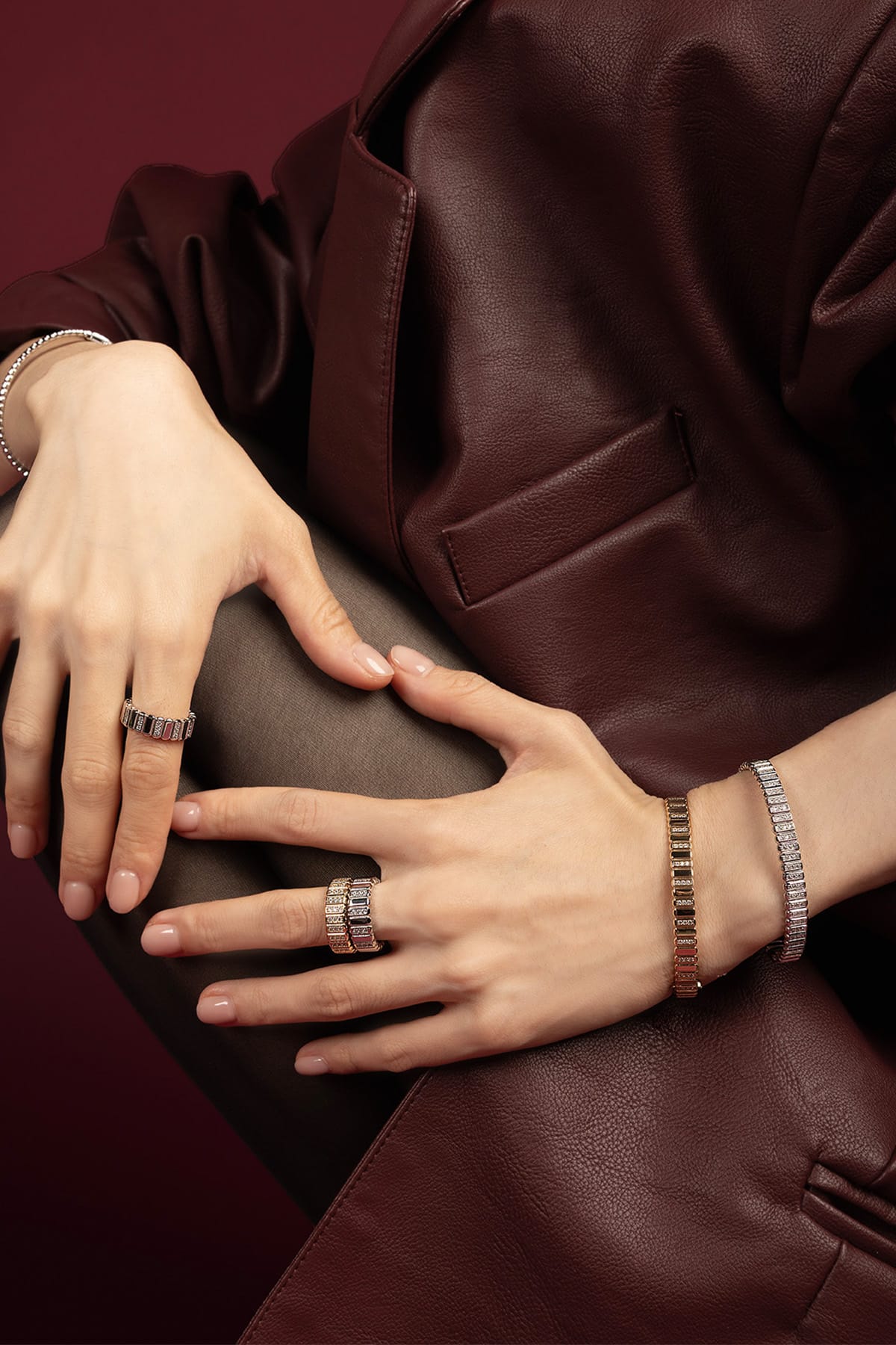 Woman wearing APM Monaco rings and bracelets, a luminous statement against rich burgundy leather.
