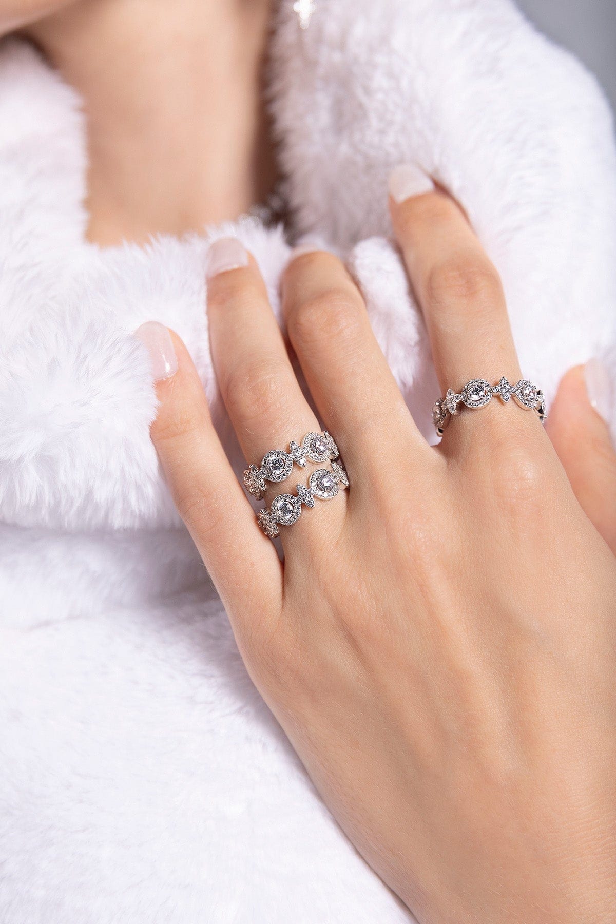Hand wearing three silver rings with a white fur background