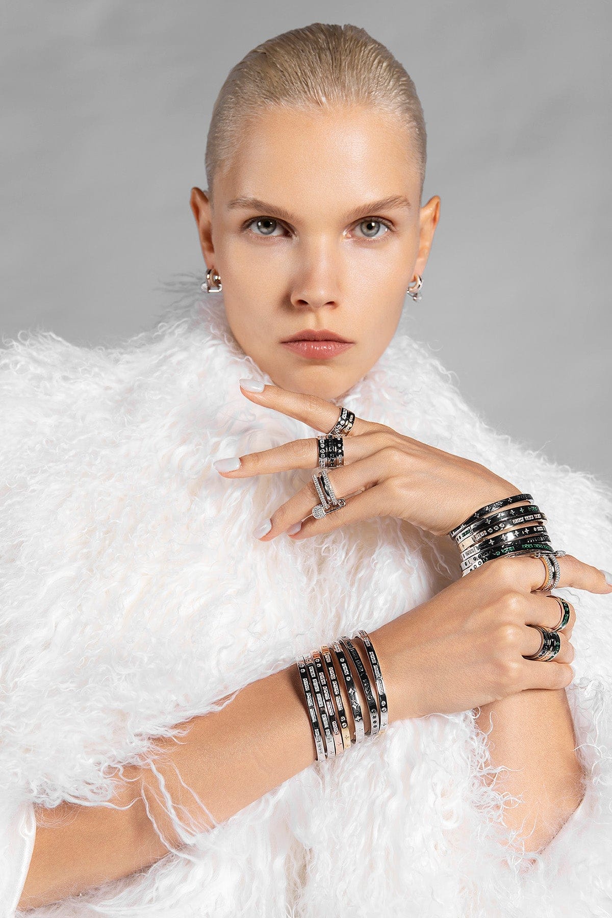 Woman wearing multiple rings and bracelets on a gray background