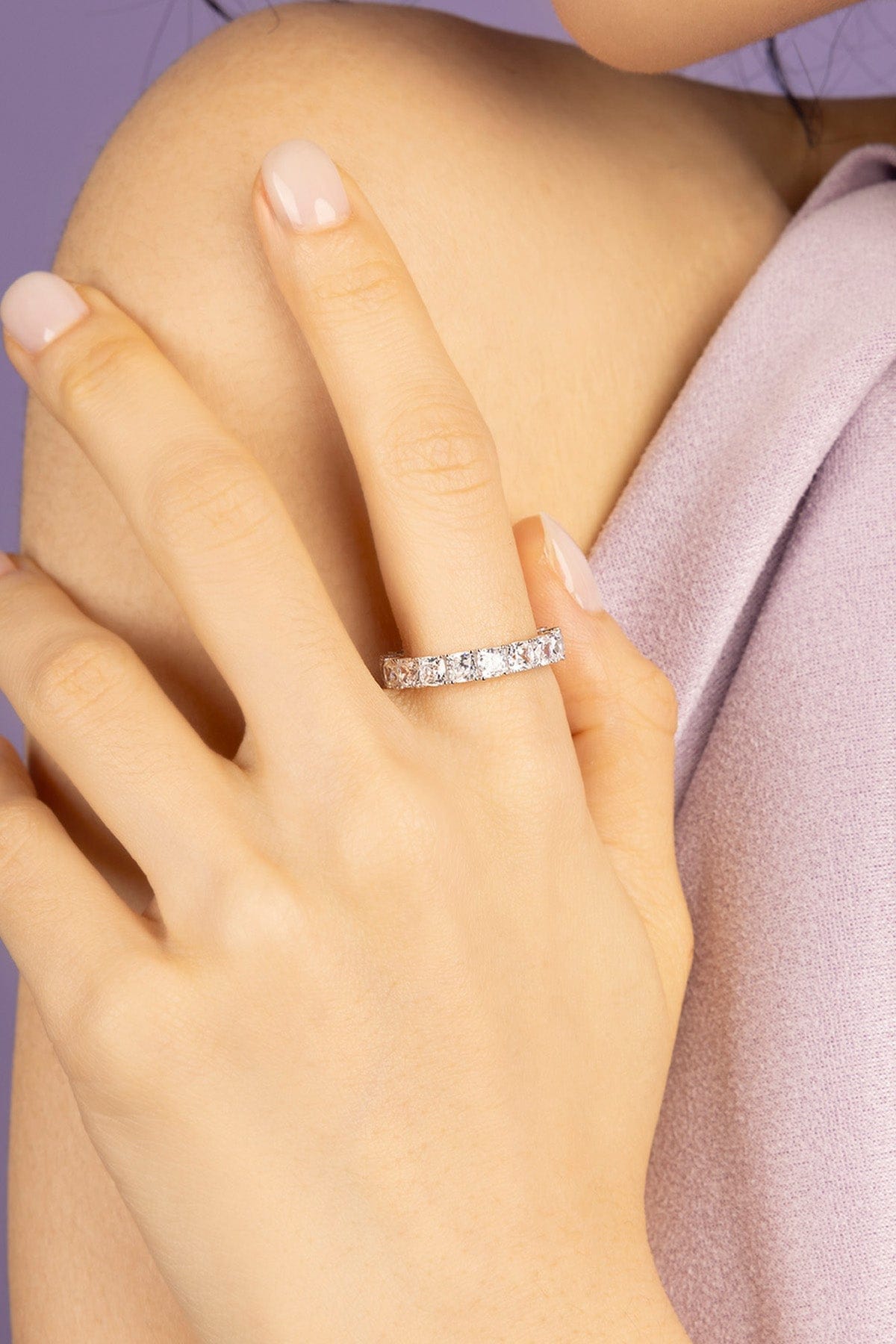 Close-up of a hand wearing a zirconia ring on a light purple background