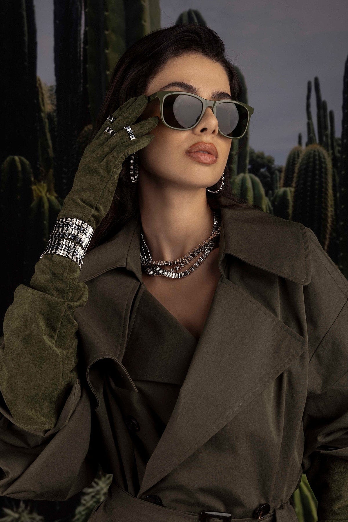 Woman in a trench coat and sunglasses with cacti in the background