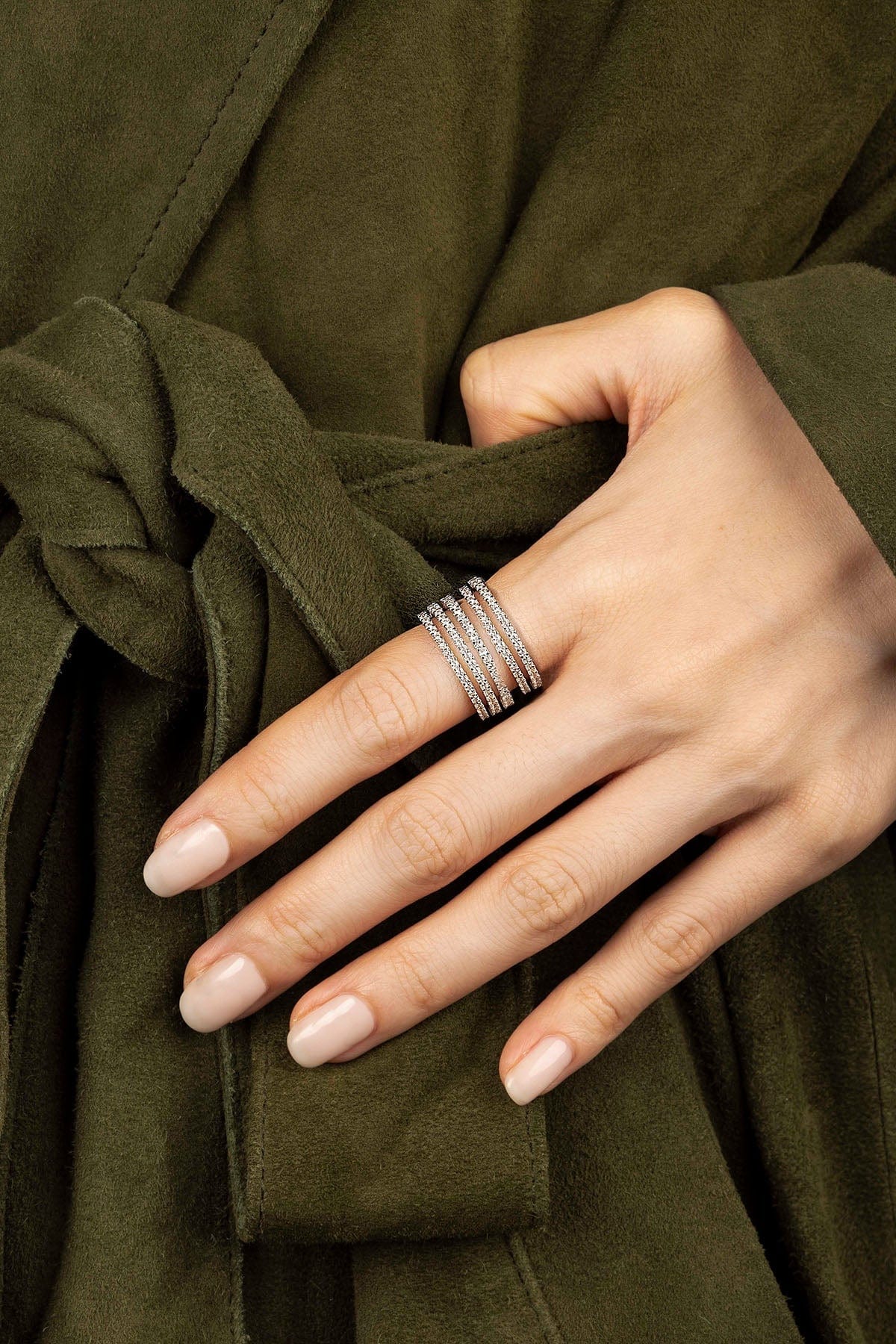 Hand wearing a silver ring with a green garment in the background