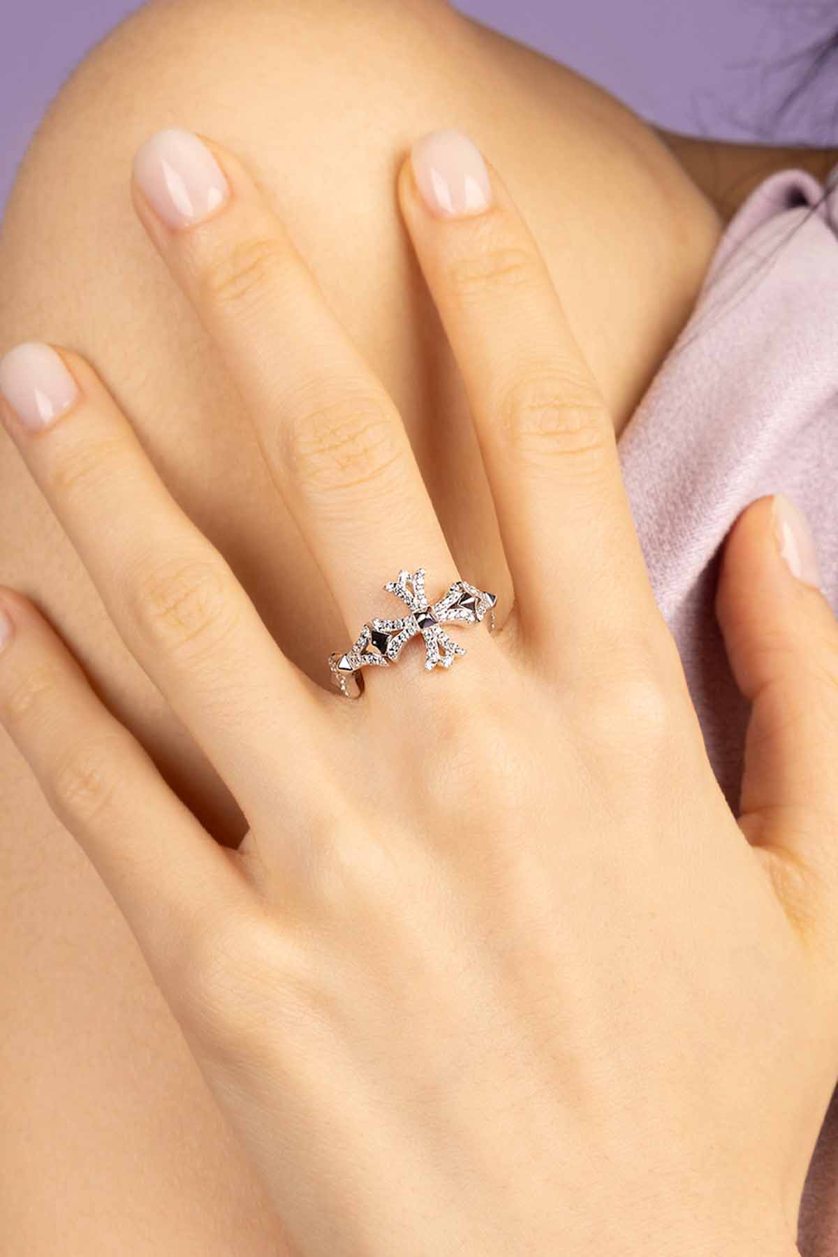 Silver-tone ring with a cross design on a hand against a purple background
