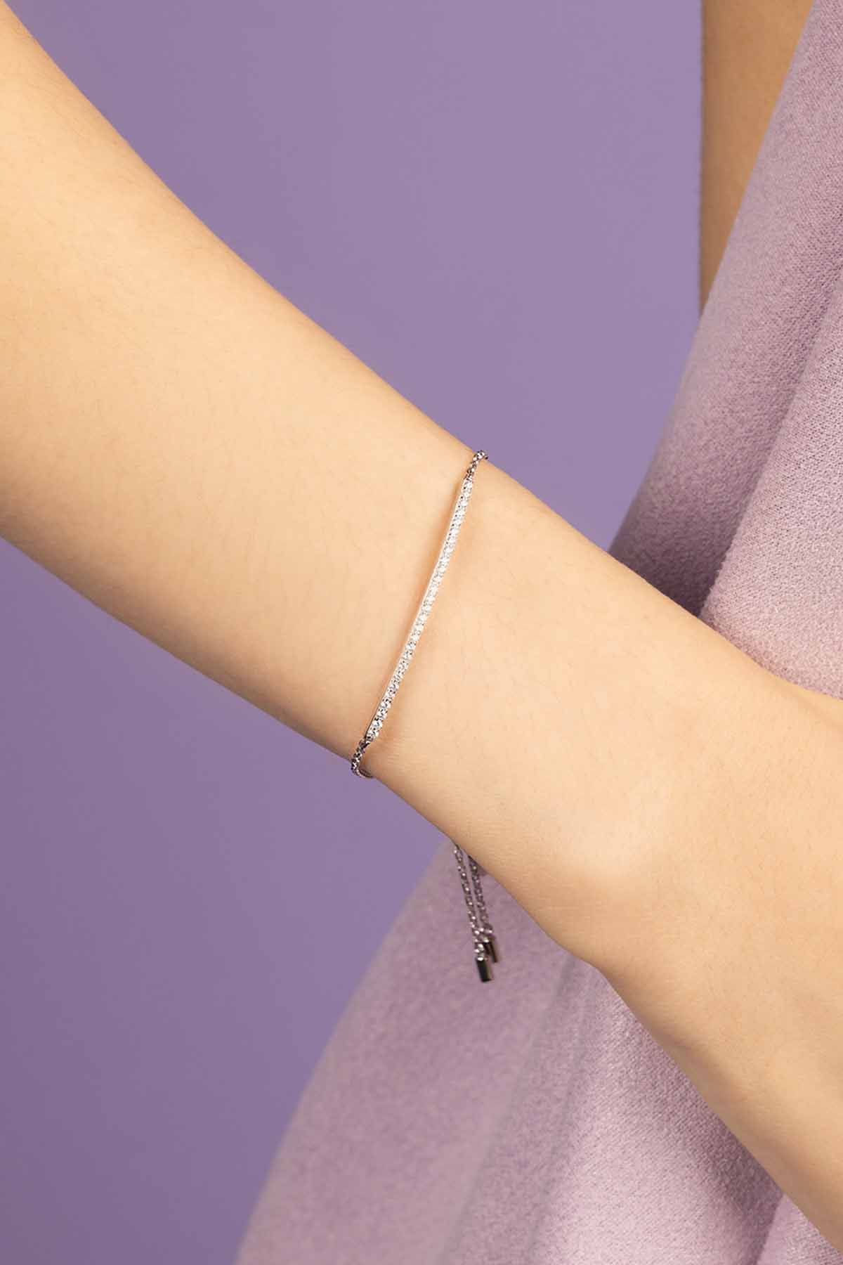 APM MONACO silver bracelet with paved line on a person's wrist against a purple background