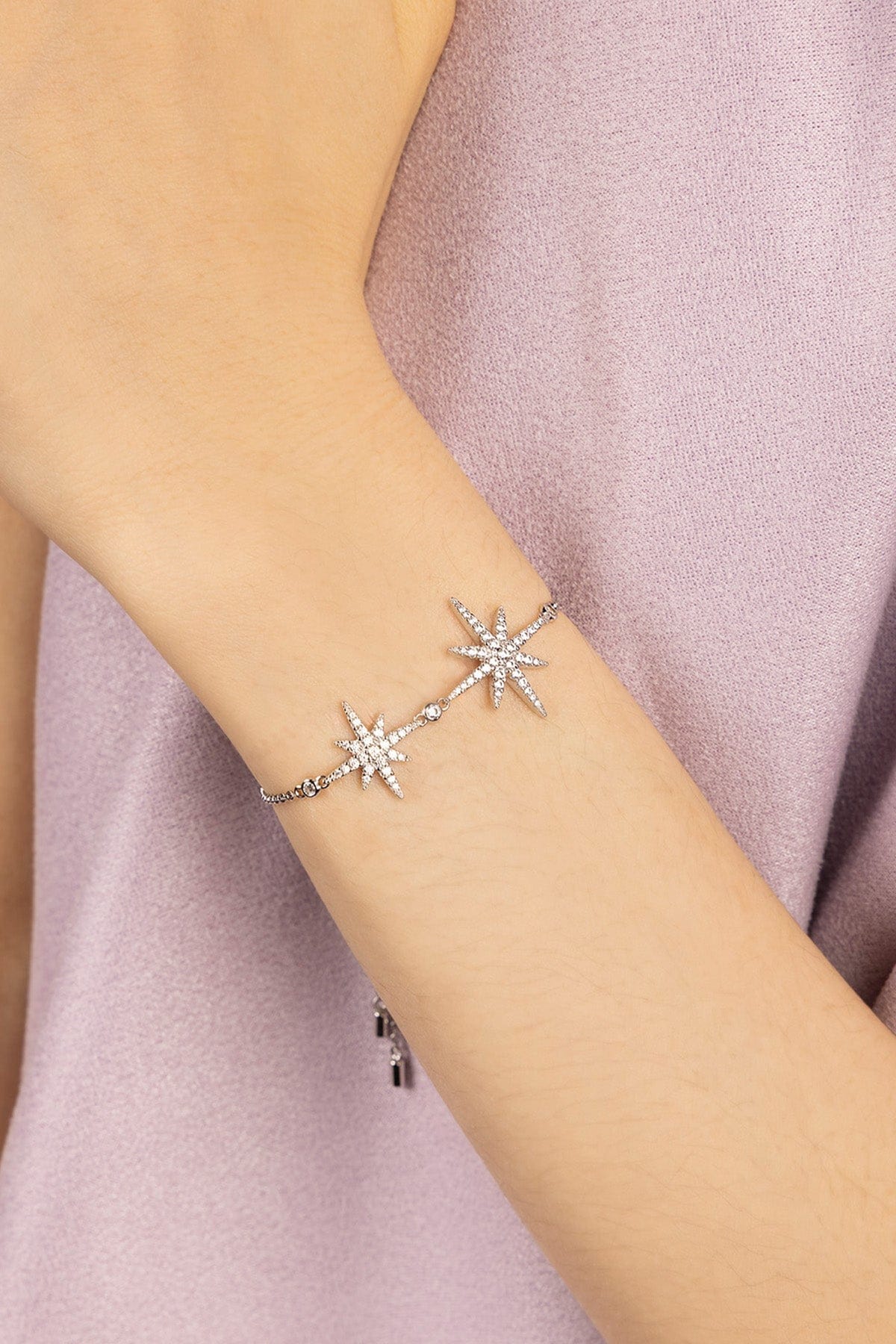 Silver star-shaped bracelet on a person's wrist with a soft pink fabric background