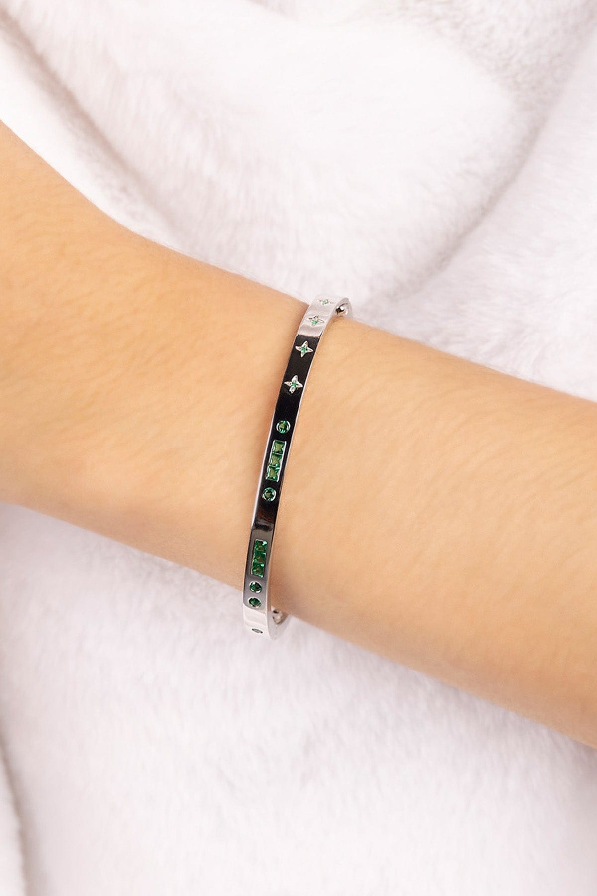 Silver bracelet with green stones on a person's wrist against a white background