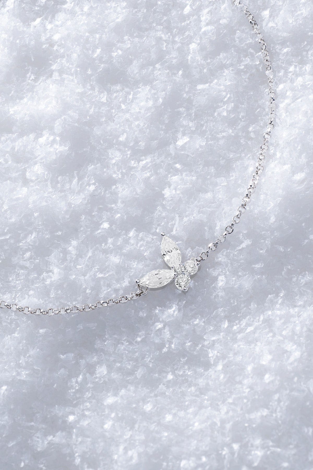 APM MONACO silver necklace with butterfly-shaped white pendant on a snowy surface