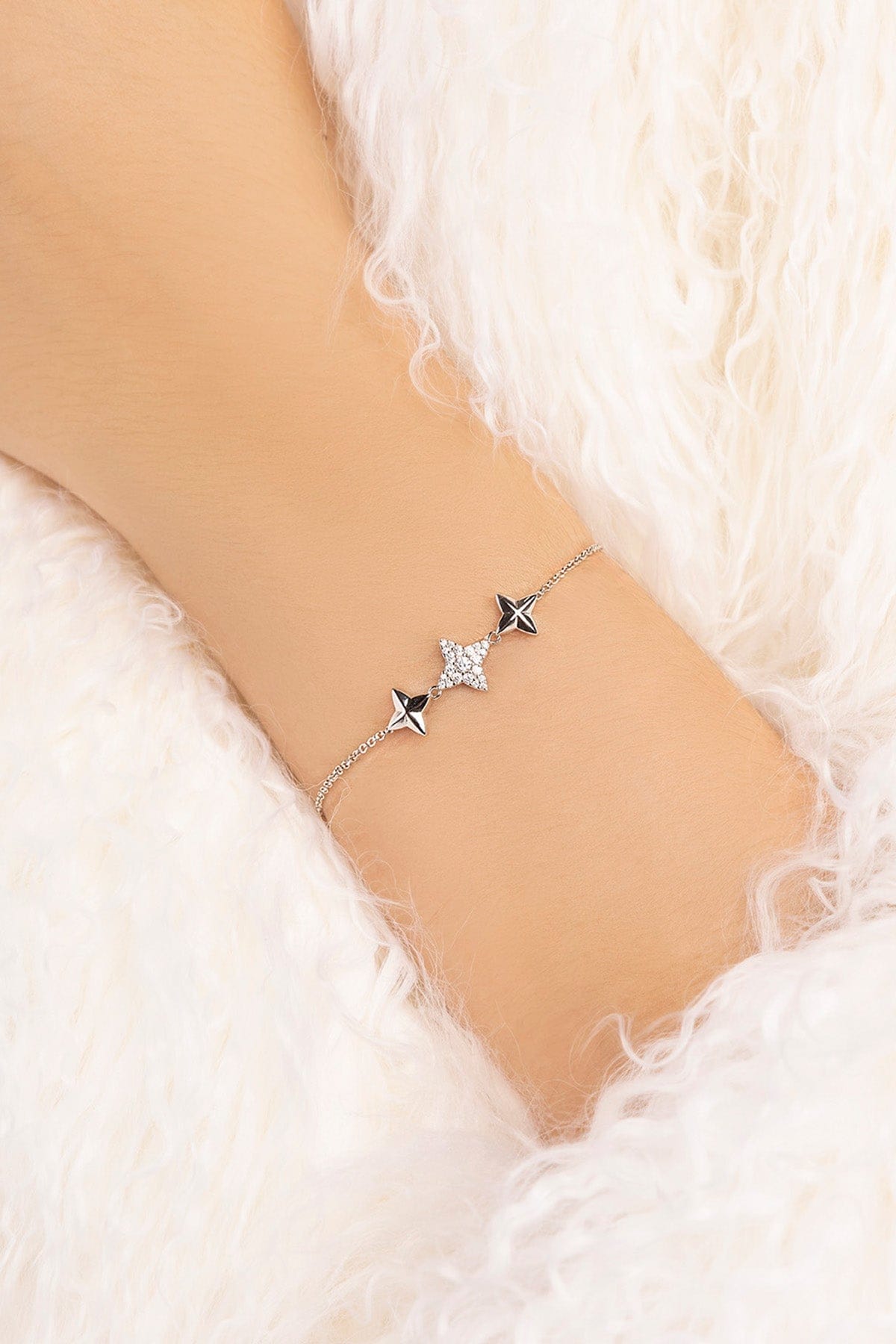Silver bracelet with star-shaped charms on a wrist against a soft white background
