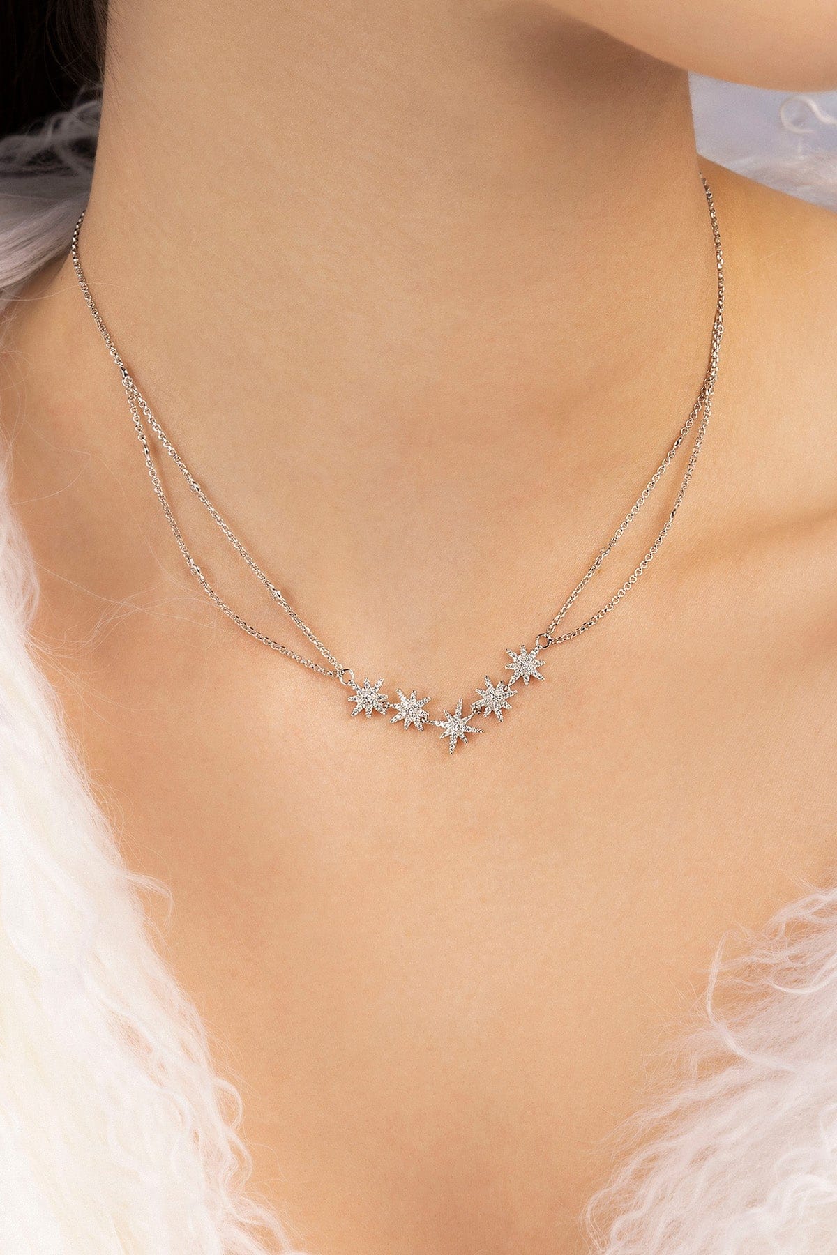 Silver star-shaped necklace on a person wearing a white feathered garment.