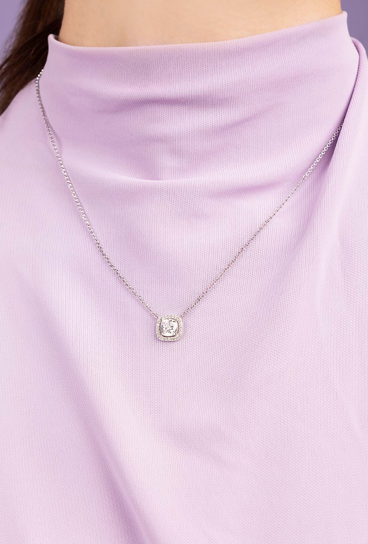 Necklace with a round pendant worn by a person in a light purple outfit.