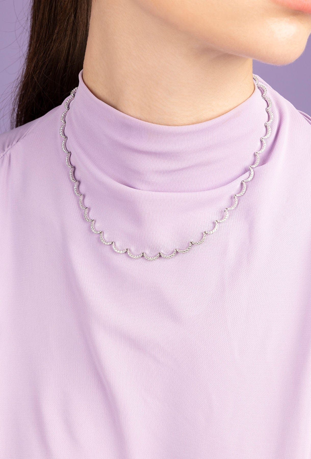 Person wearing APM MONACO silver wavy adjustable necklace on a light purple background