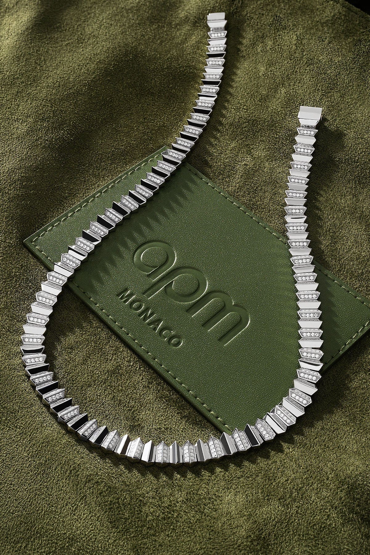 Silver necklace on a green textured surface with 'qpm Monaco' logo