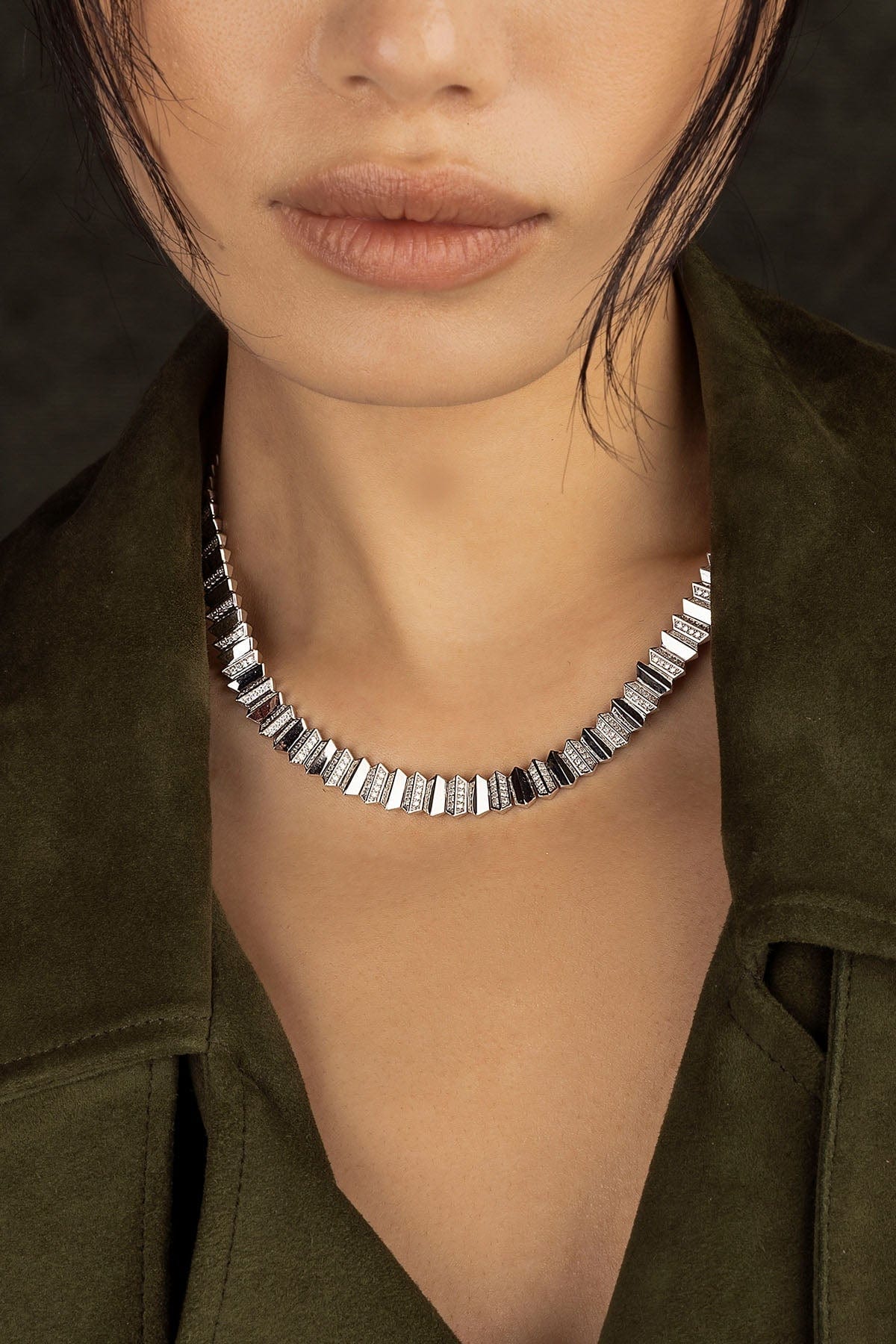 Close-up of a model wearing a silver necklace with a dark background