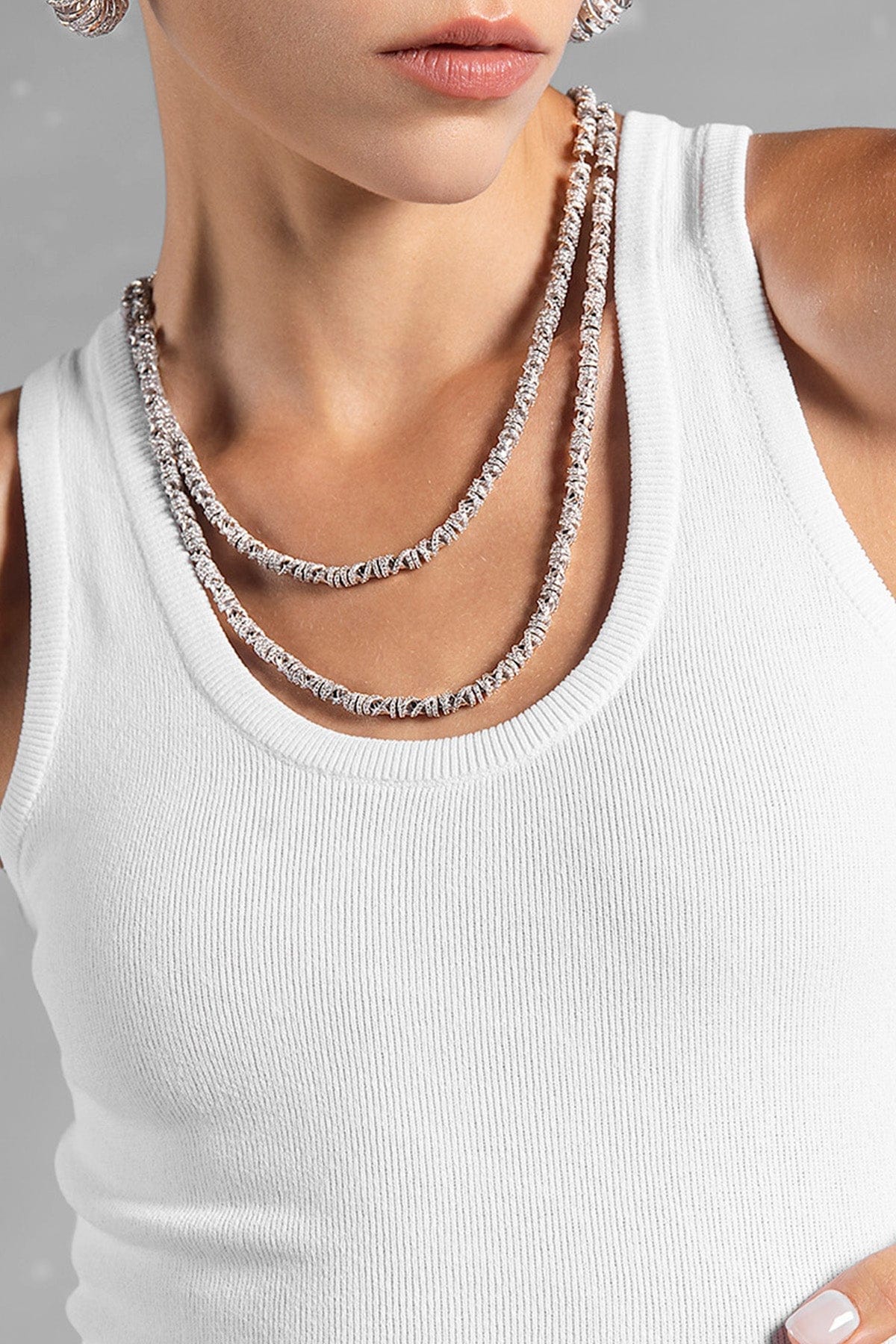 Close-up of a model wearing a white tank top with APM MONACO enlace necklace in silver
